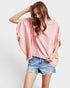 Woman wearing a pink oversized top and denim shorts on a white background