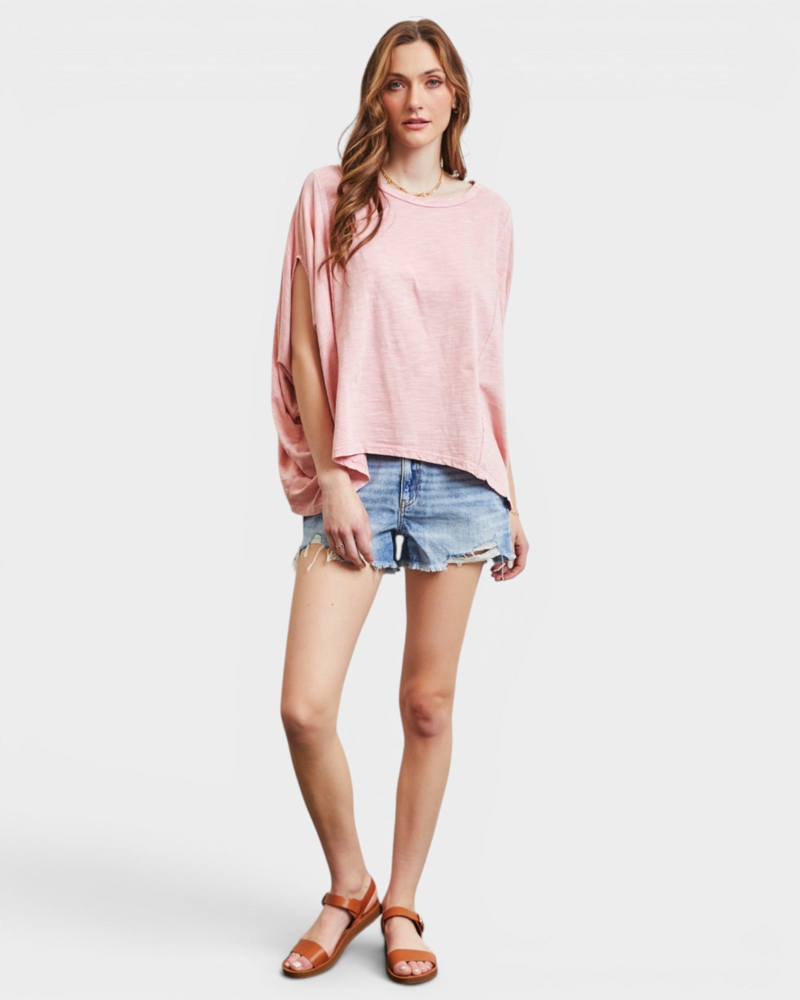 Woman wearing a pink oversized top and denim shorts on a white background