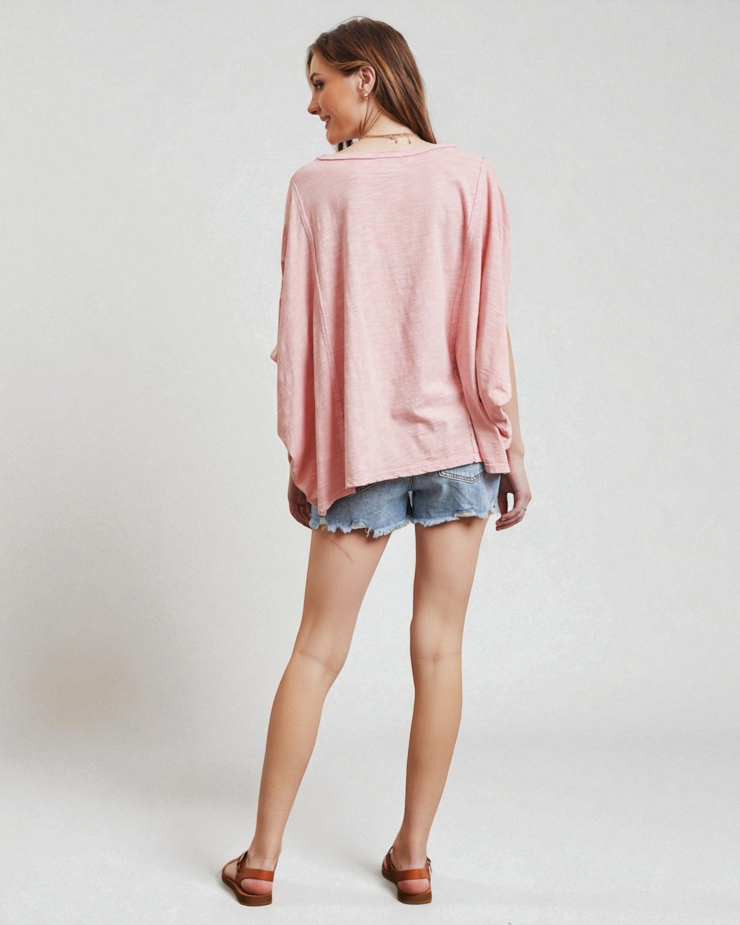 Woman wearing a pink oversized sweater and denim shorts on a white background