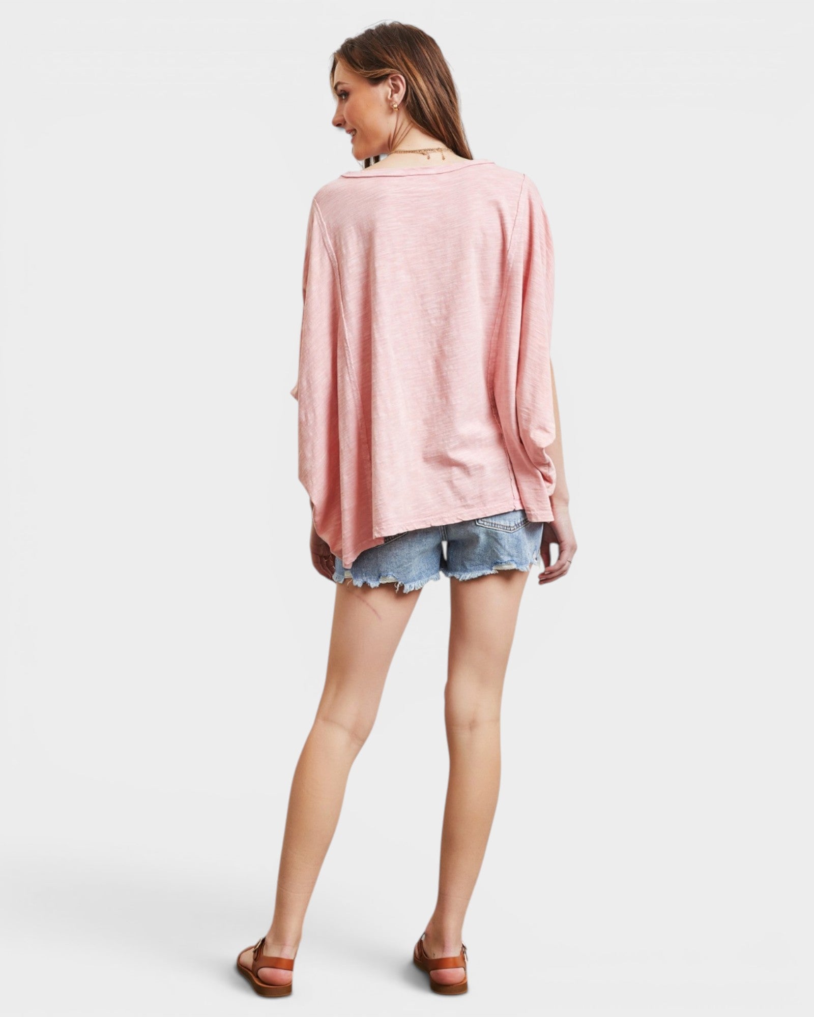 Woman wearing a pink oversized shirt and denim shorts on a white background