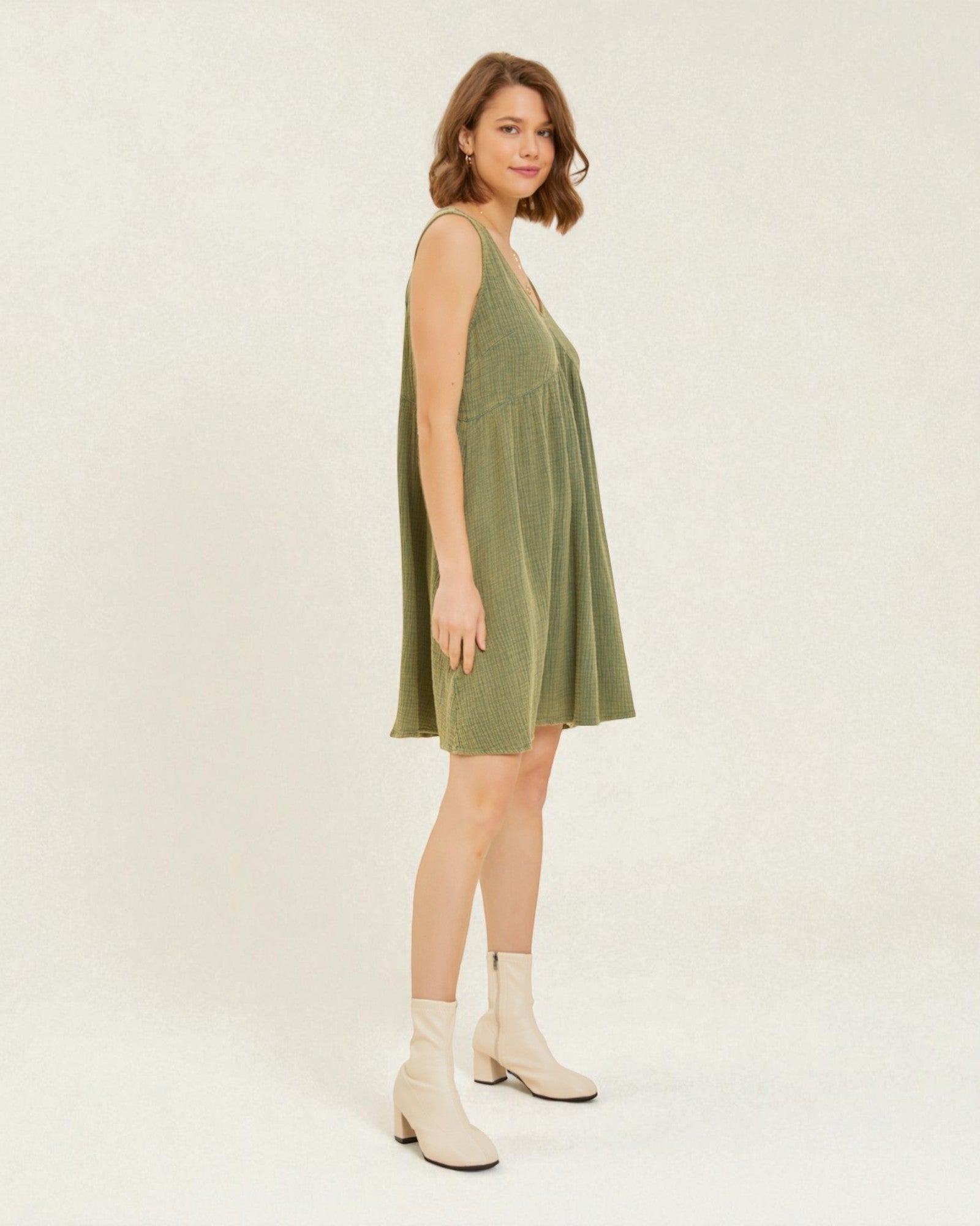 Woman wearing a green dress with white boots on a plain background