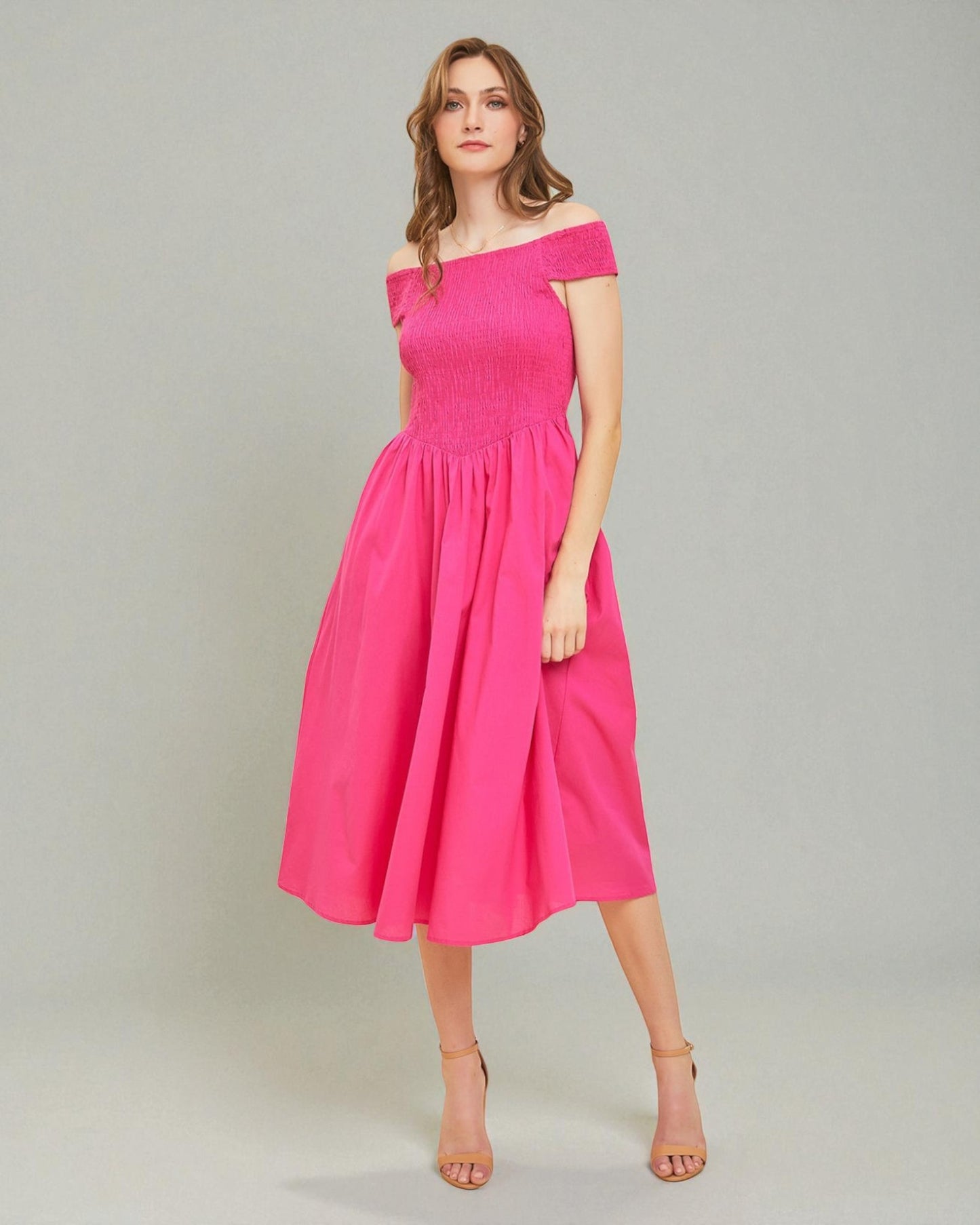 Woman wearing a bright pink off-shoulder dress on a plain background