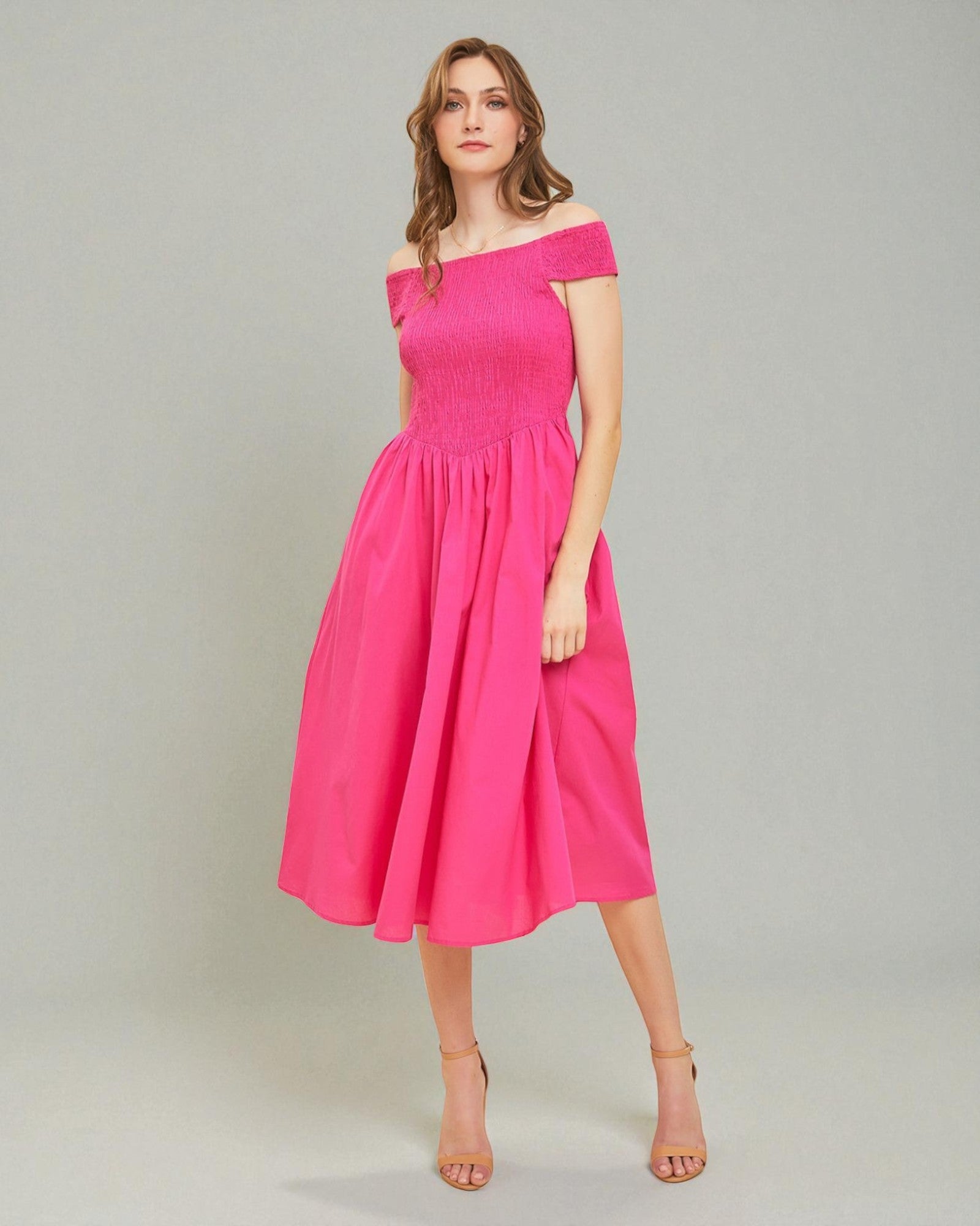 Woman wearing a bright pink off-shoulder dress on a plain background