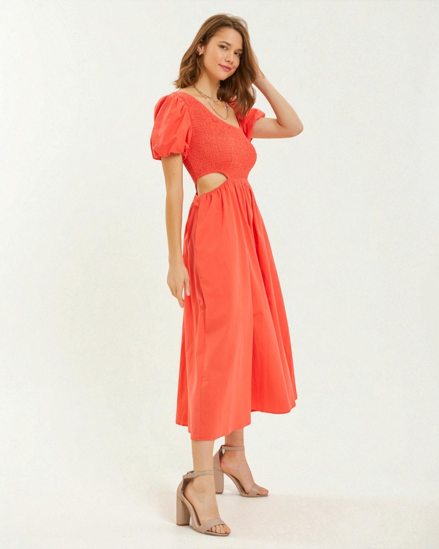 Woman wearing a coral dress with cut-out design on a white background