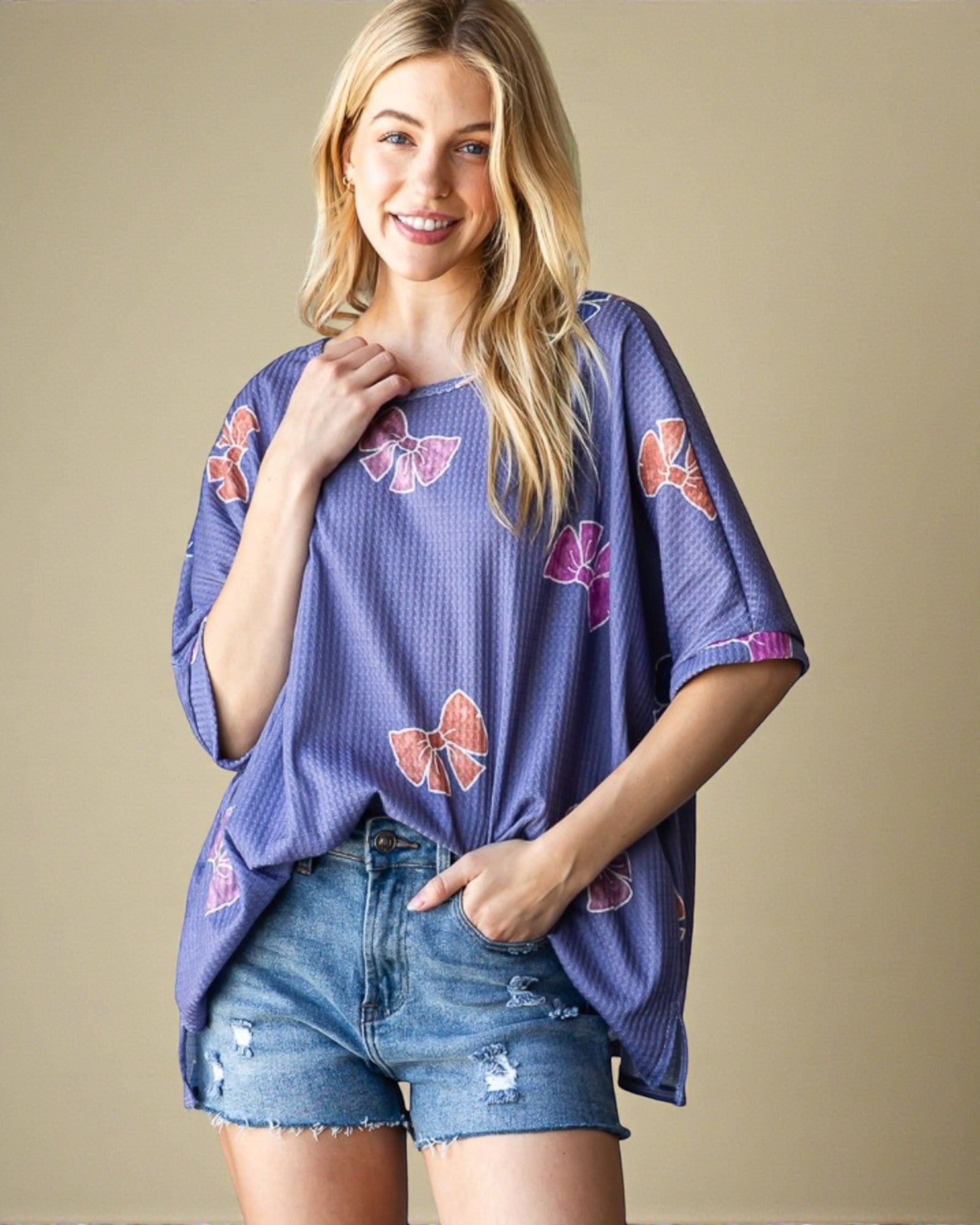 Woman wearing a purple top with butterfly patterns and denim shorts on a beige background