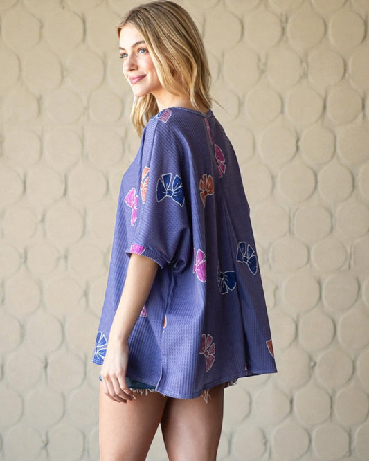 Woman wearing a blue kimono-style garment with floral patterns against a textured beige wall.