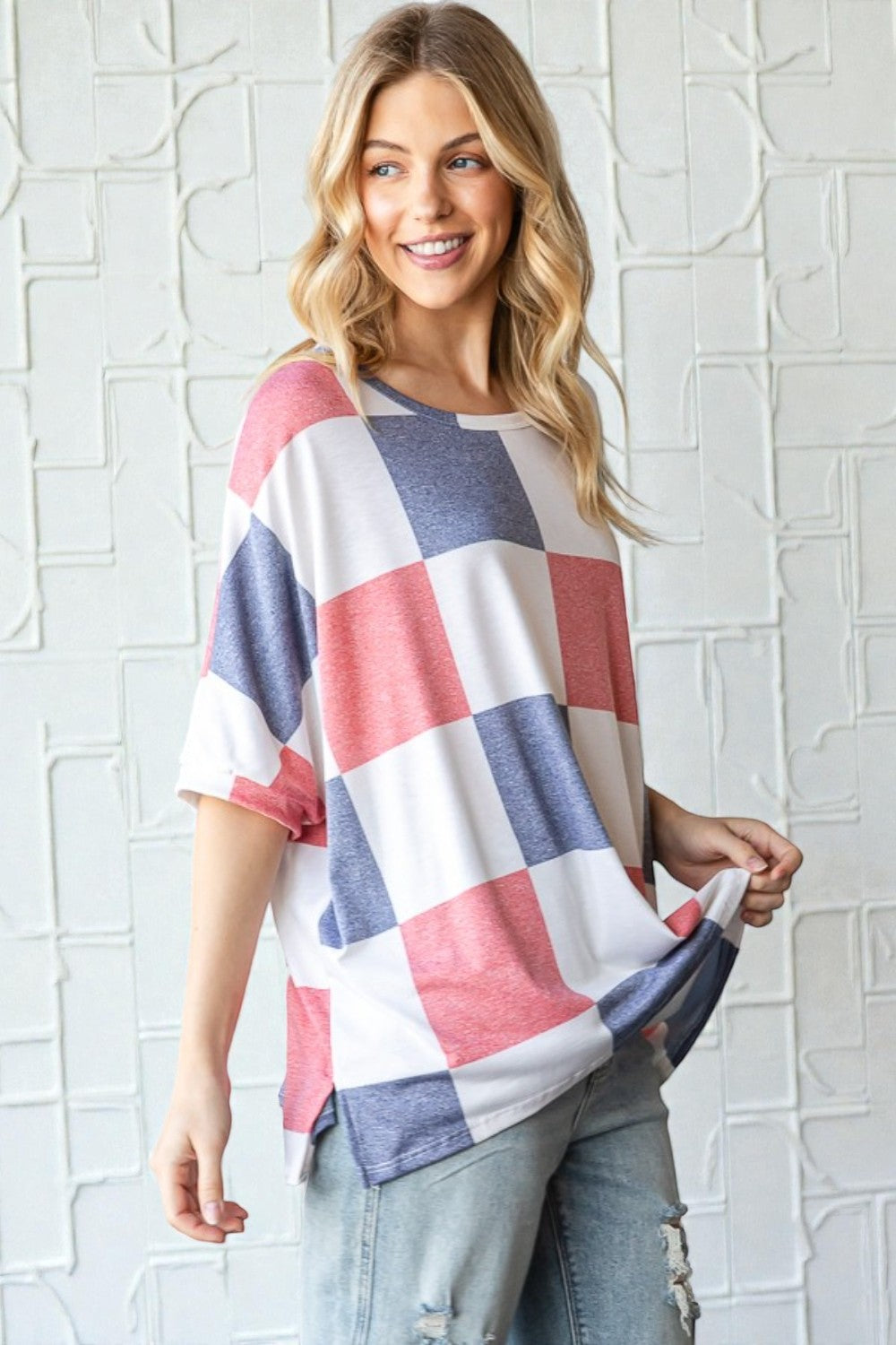 Woman wearing a colorful checkered shirt against a white brick wall.