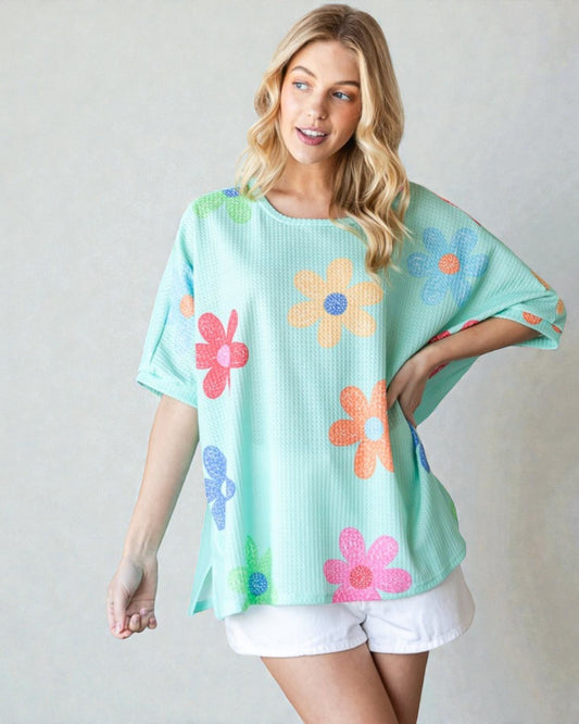 Woman wearing a light blue oversized shirt with colorful flower patterns on a plain background