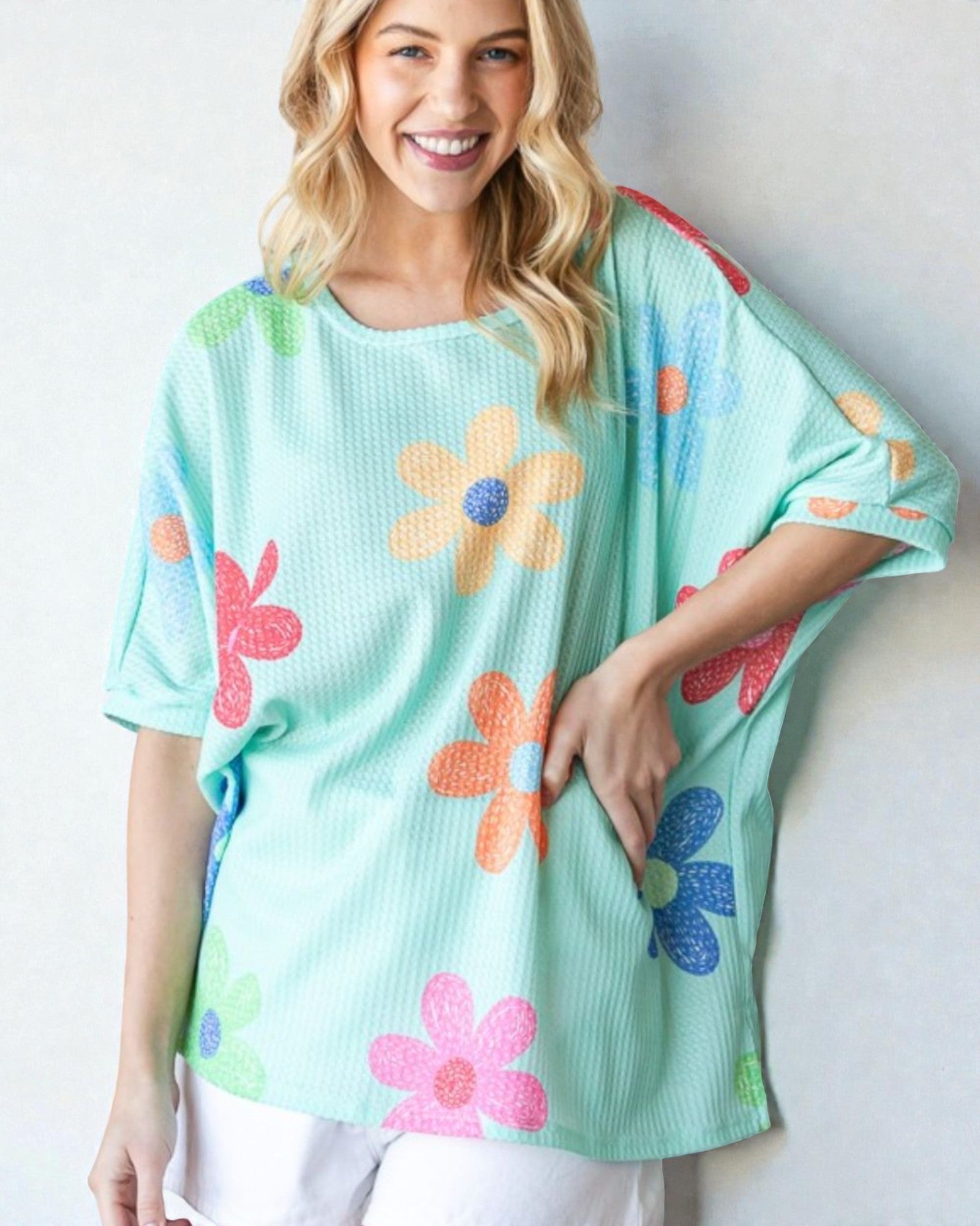 Woman wearing a light blue sweater with colorful flower patterns on a plain background