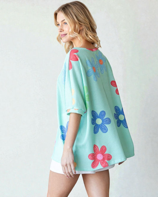 Woman wearing a light blue poncho with colorful flower patterns on a white background