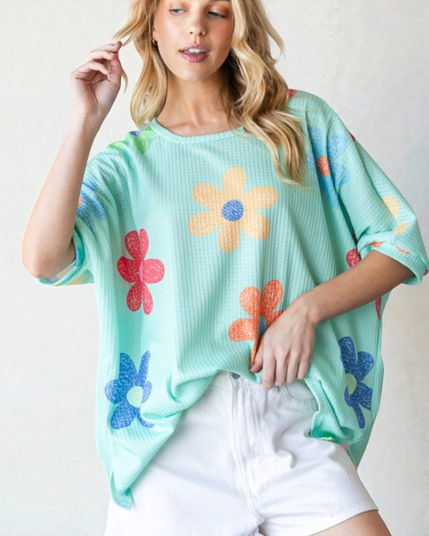 Woman wearing a light blue oversized sweater with colorful floral patterns on a plain background