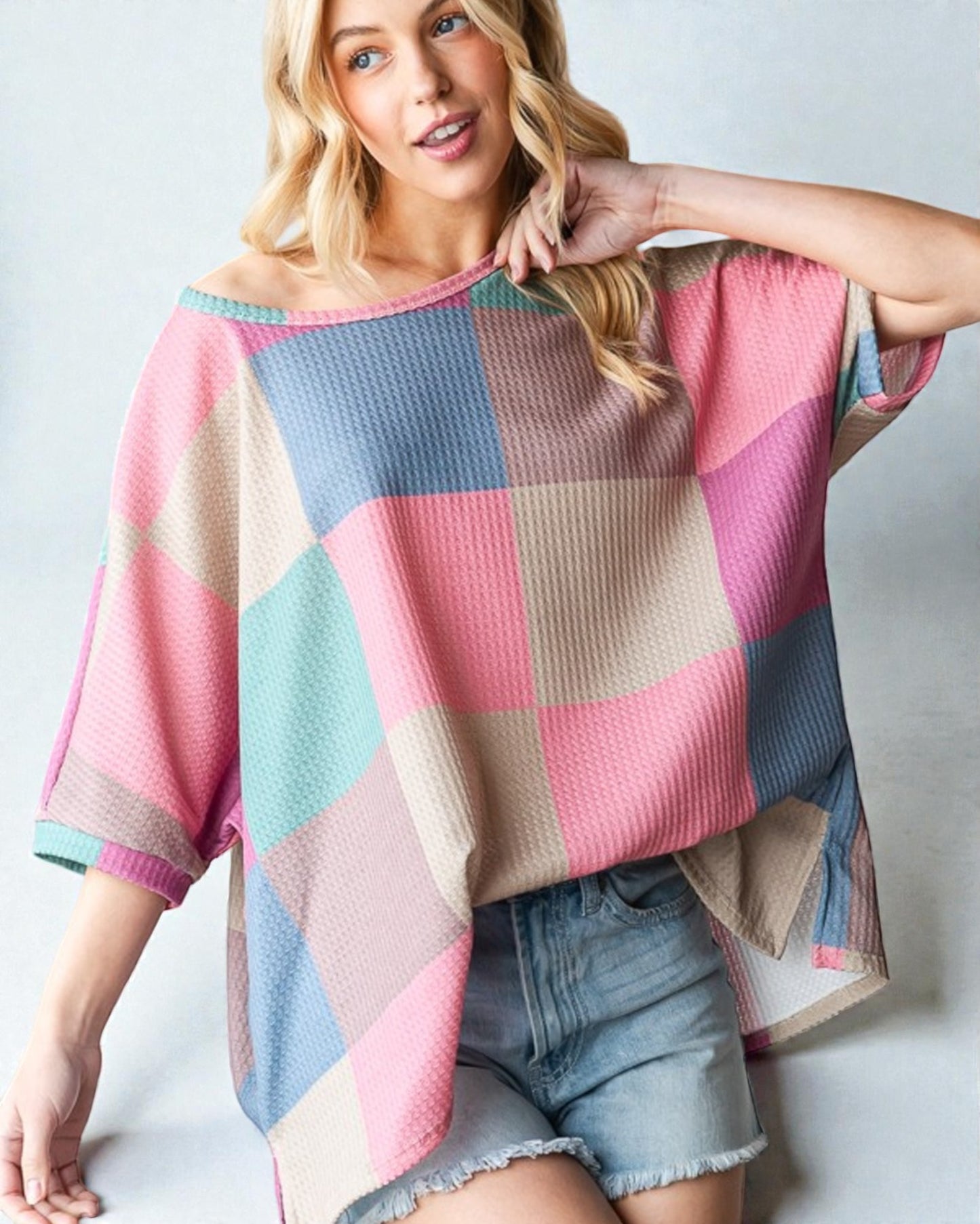 Woman wearing a colorful checkered sweater and denim shorts against a plain background