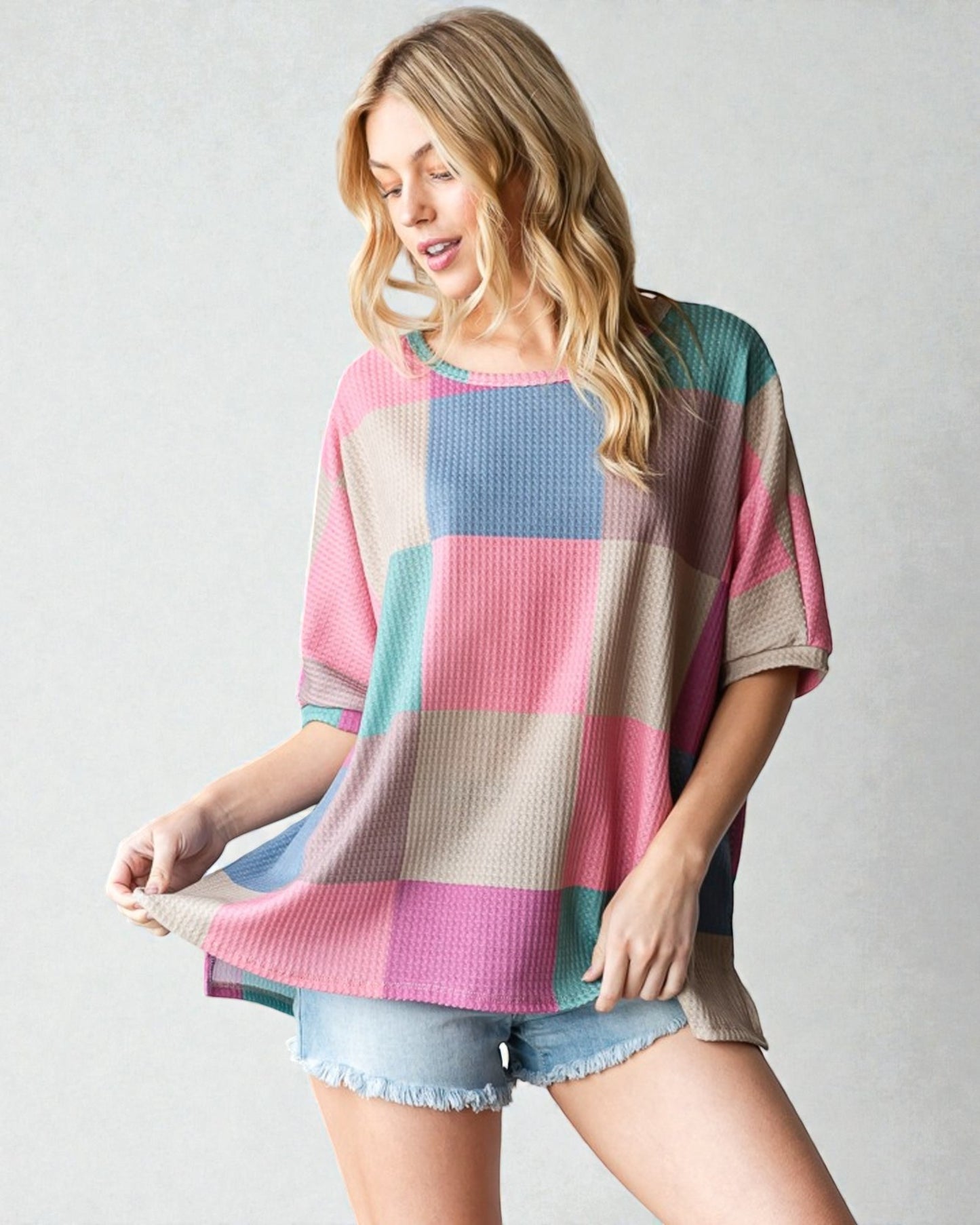 Woman wearing a colorful checkered top and denim shorts on a plain background