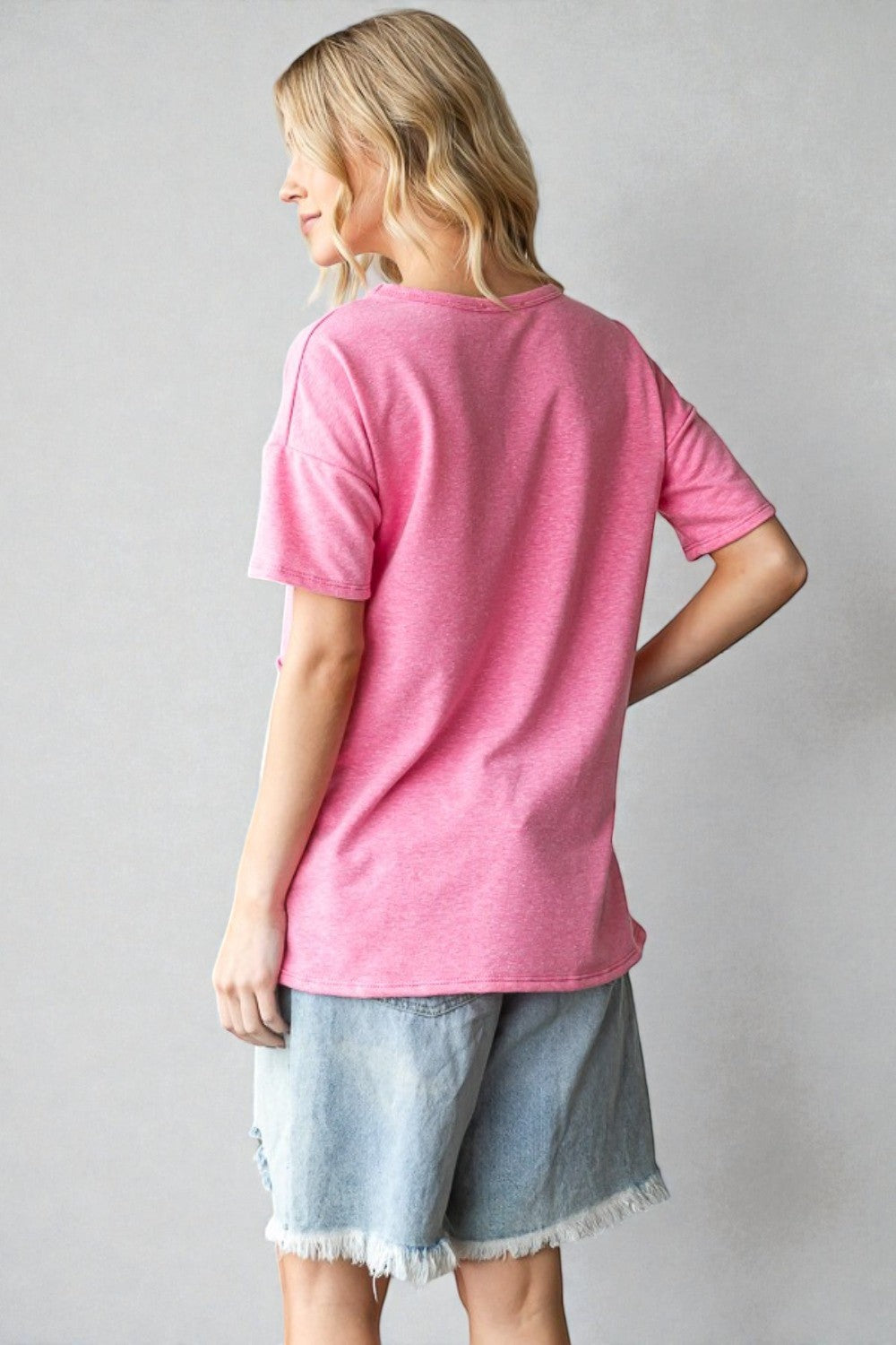 Person wearing a pink t-shirt and denim shorts against a plain background