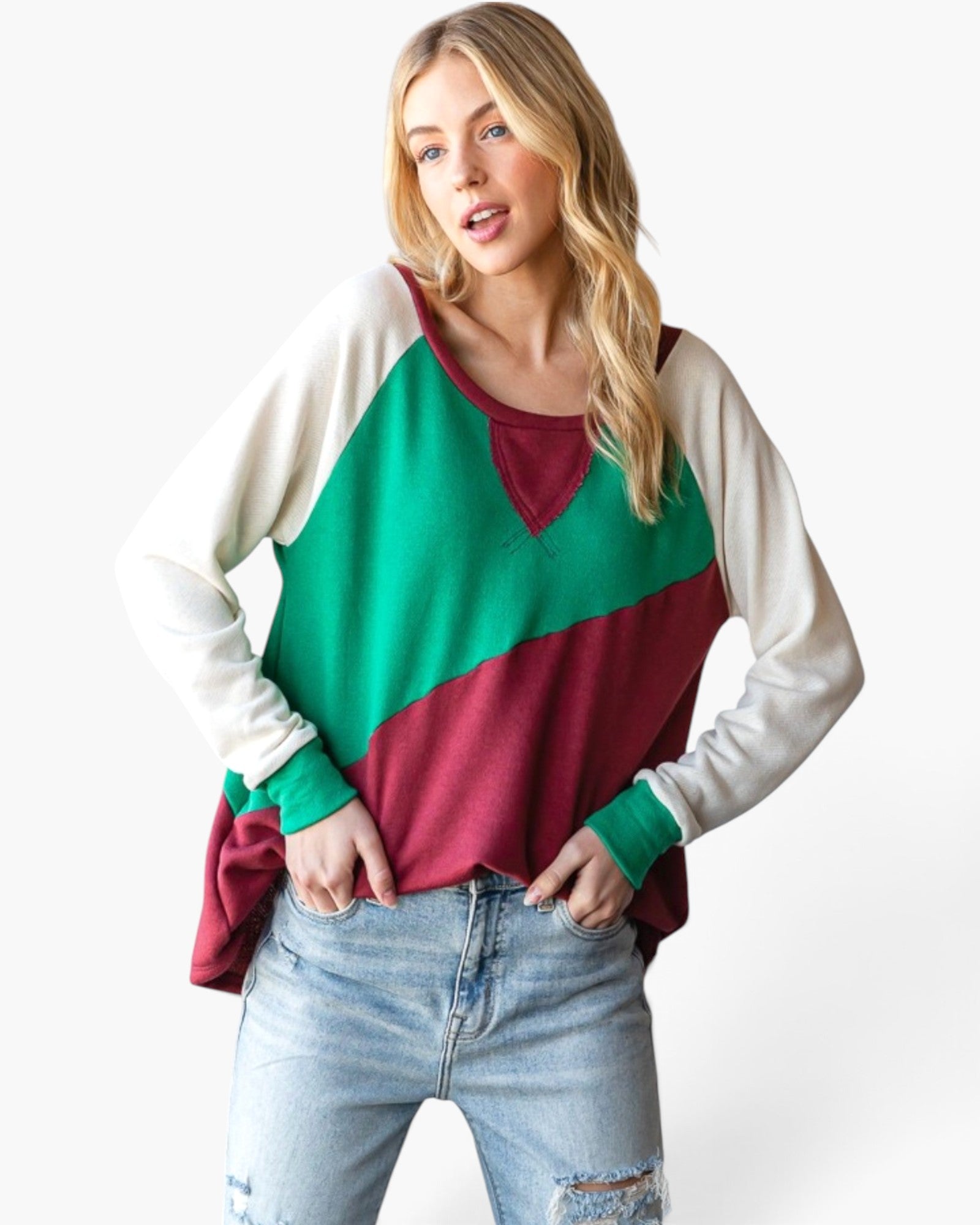 A woman modeling a long-sleeve colorblock sweater with cream, green, and burgundy panels, paired with light-wash distressed jeans against a plain white background.