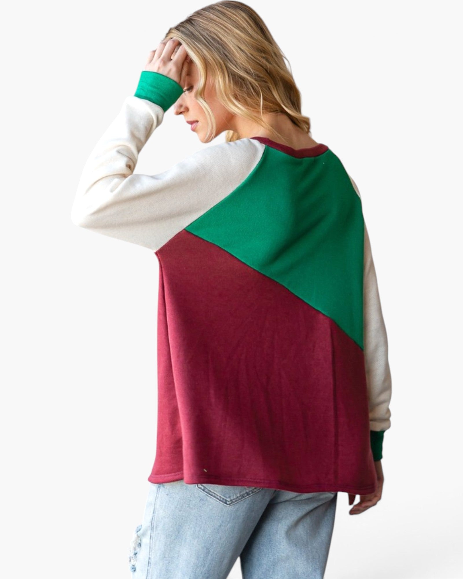 A woman wearing a colorblock long-sleeve top with cream, green, and burgundy panels, paired with light blue jeans, shown from a side-back angle against a plain white background.