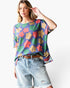 A woman modeling a short-sleeve waffle-knit top with a colorful floral pattern in purple, green, orange, and yellow, paired with light-wash denim shorts and a brown belt against a plain white background.