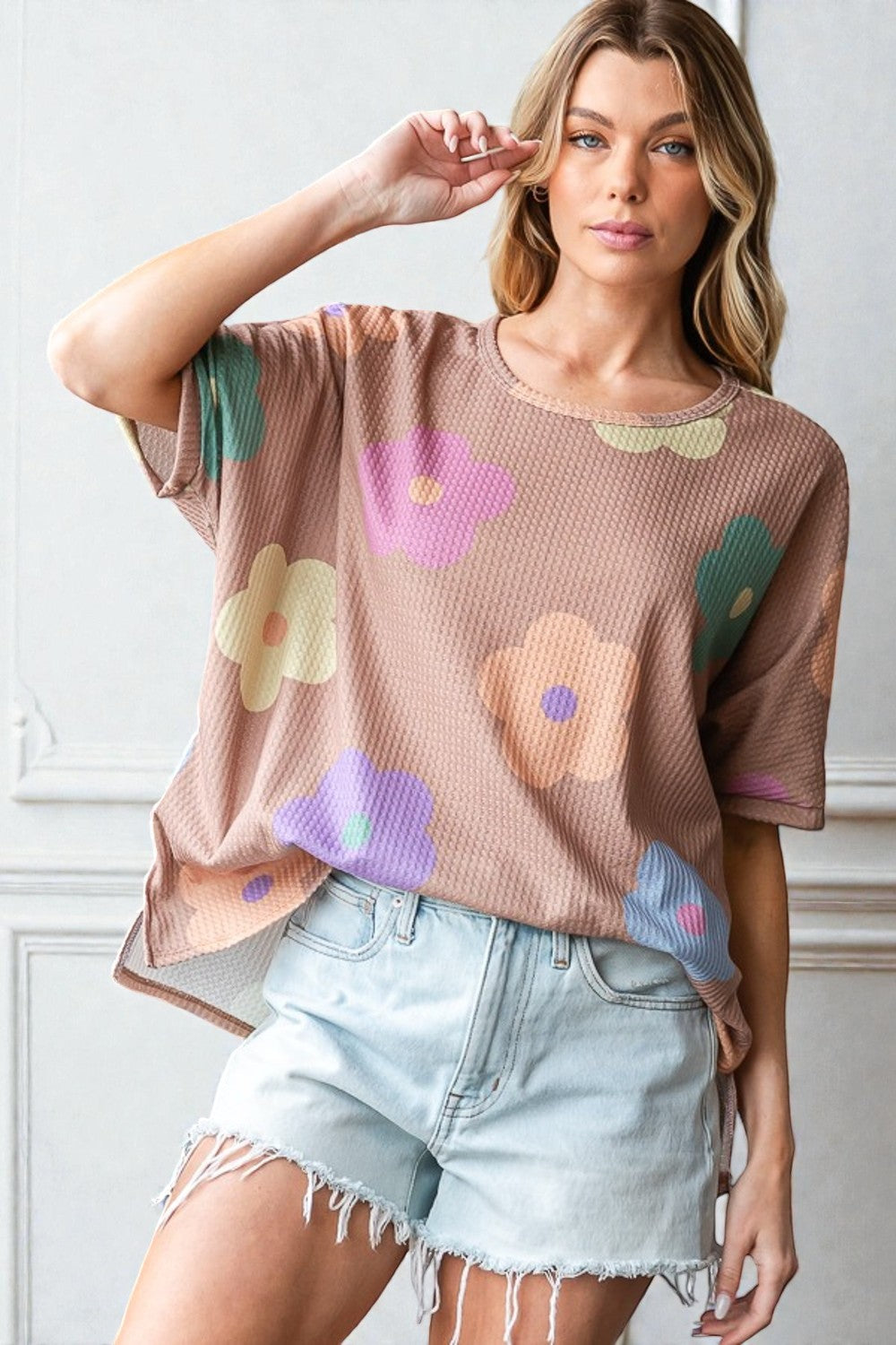 Woman wearing a brown oversized t-shirt with colorful floral patterns and light blue denim shorts.