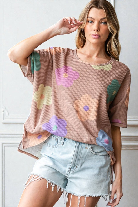 Woman wearing a brown oversized t-shirt with colorful floral patterns and light blue denim shorts.