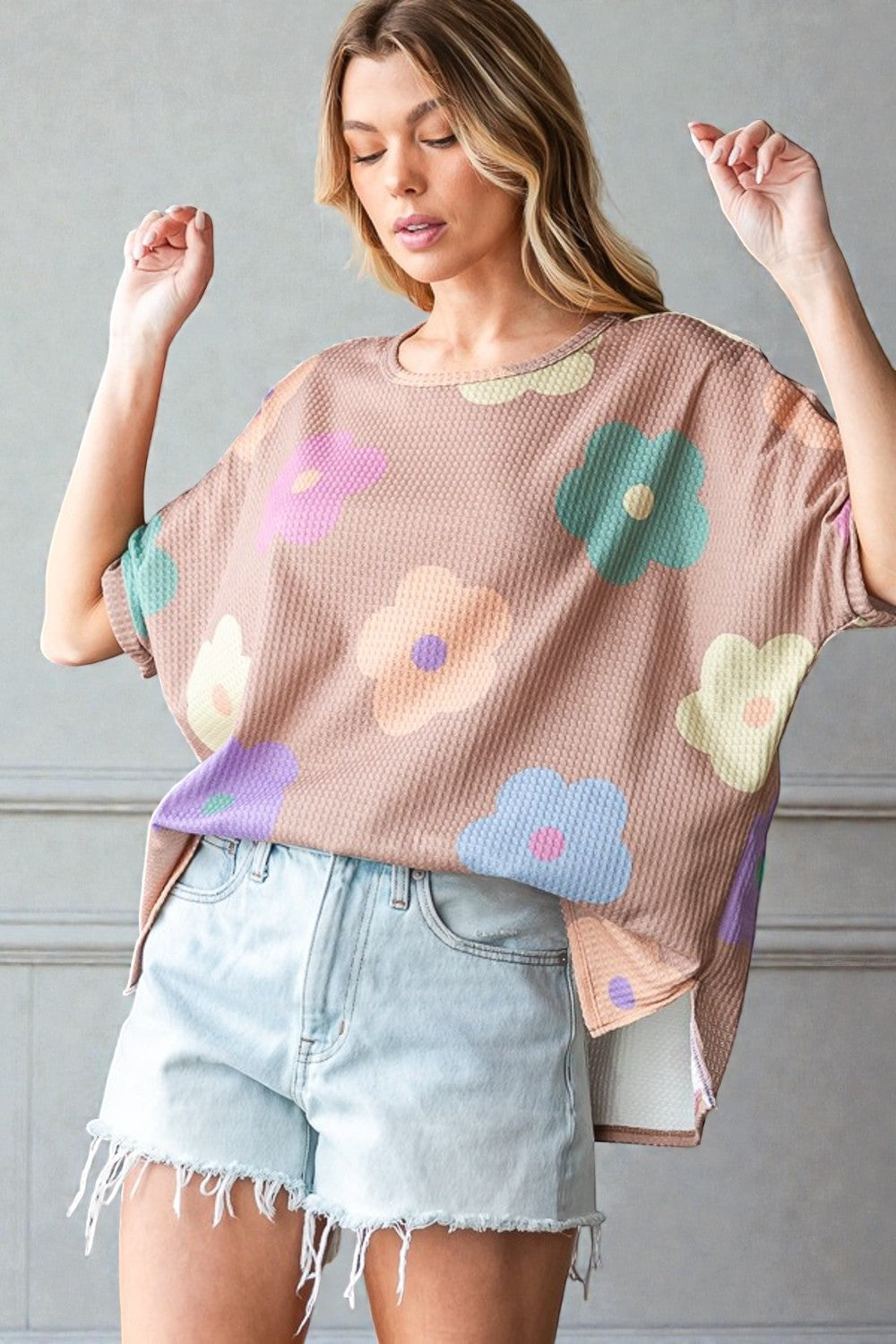 Woman wearing a floral-patterned top and denim shorts against a gray background