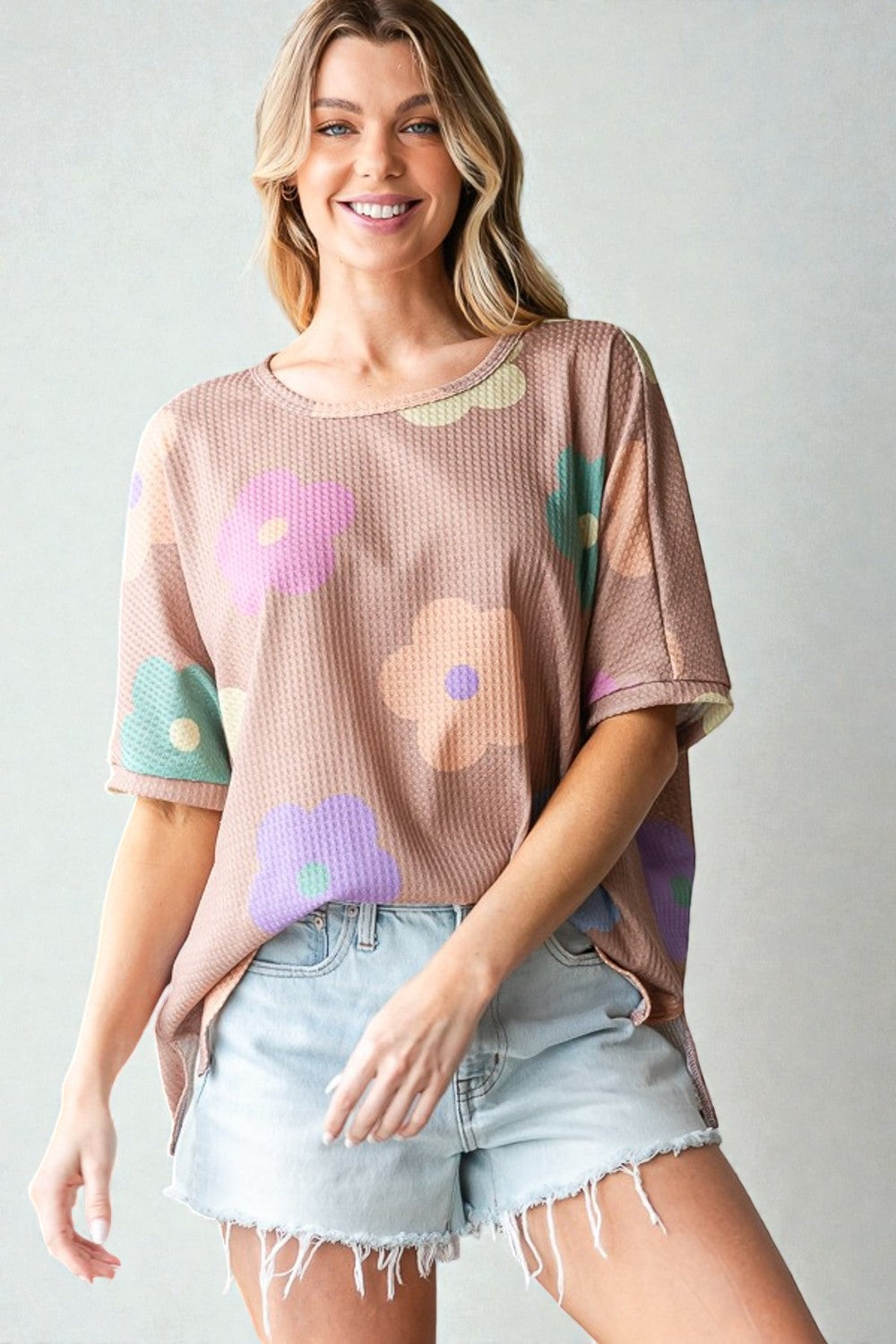 Woman wearing a floral patterned top and denim shorts on a plain background