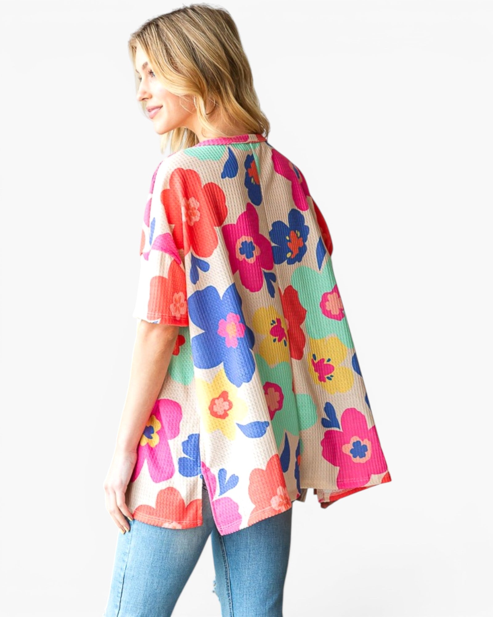 A woman wearing a short-sleeve waffle-knit top with a colorful floral pattern, paired with blue jeans, photographed against a plain white background.
