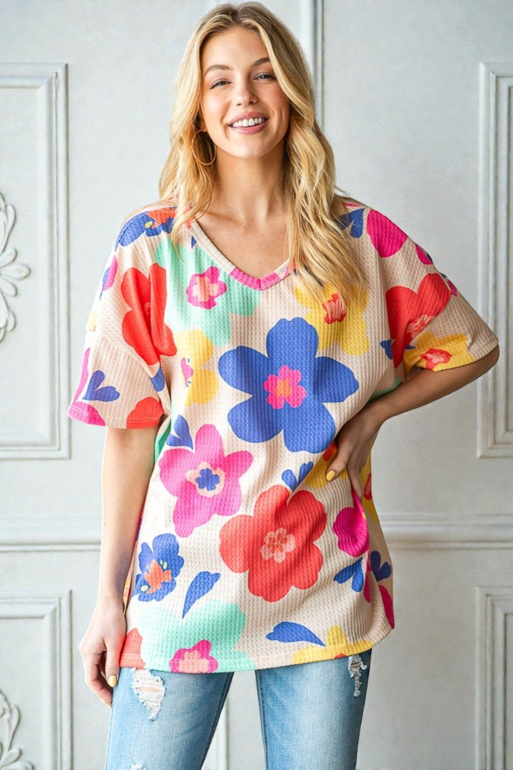 Woman wearing a colorful floral top against a white wall