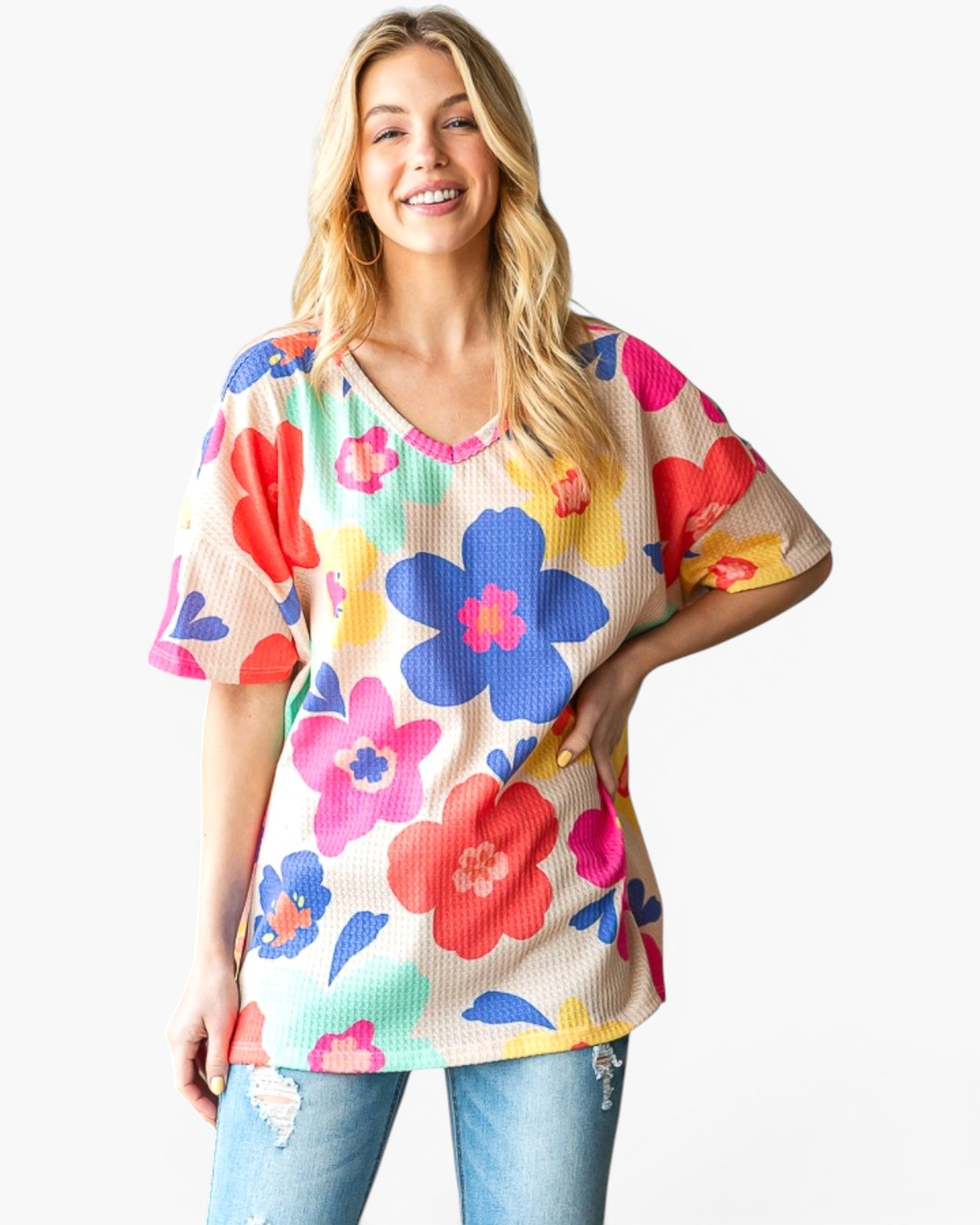 A woman wearing a short-sleeve waffle-knit top with a colorful floral pattern, paired with light-wash distressed jeans, against a plain white background.