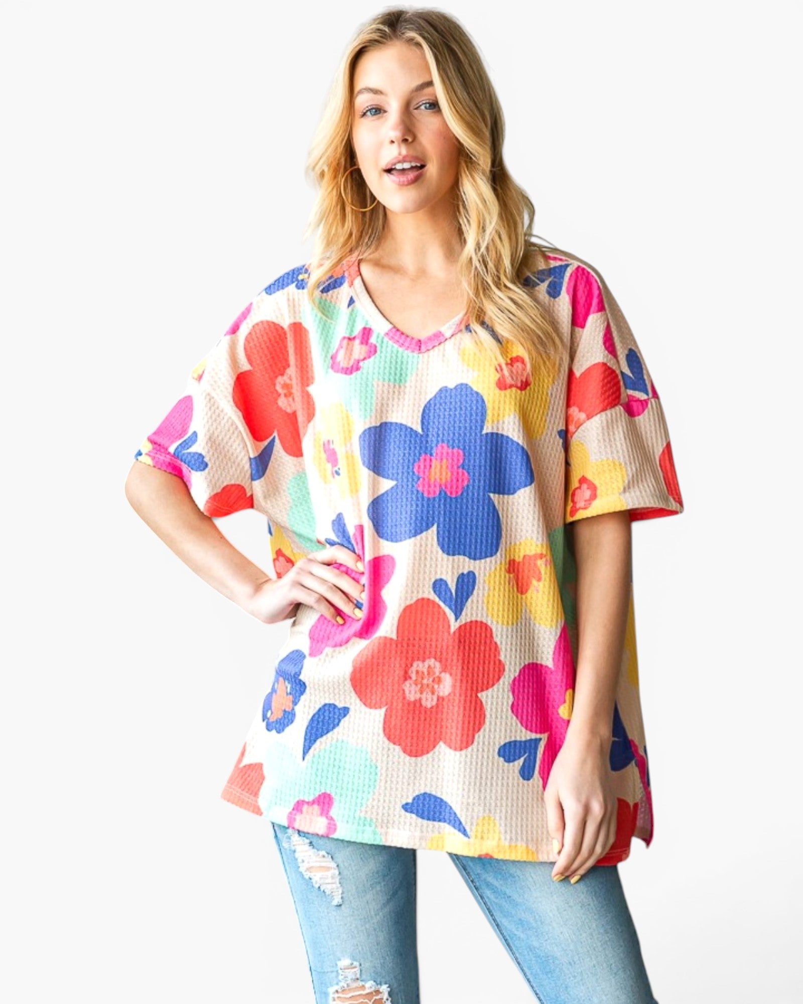 A woman modeling a short-sleeve waffle-knit top with a colorful floral print, paired with distressed blue jeans, against a plain white background.