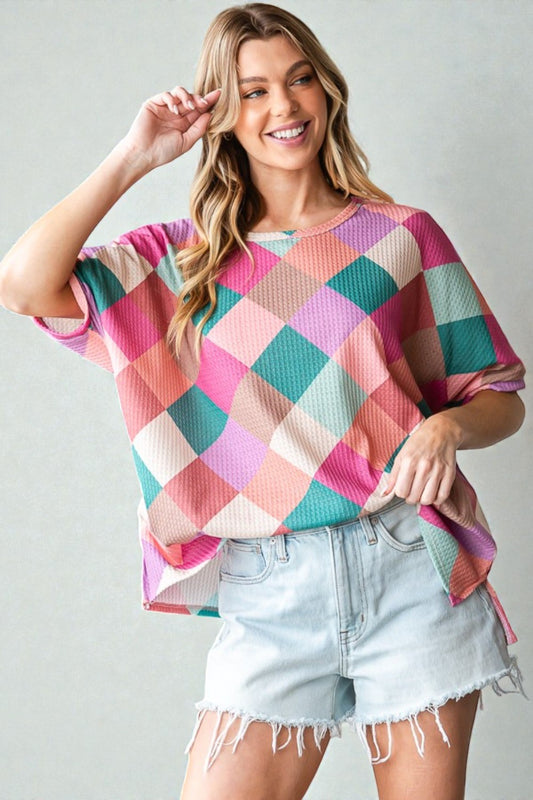 Woman wearing a colorful checkered top and denim shorts on a plain background