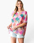 A woman modeling a short-sleeve waffle-knit top with a colorful geometric diamond pattern in pink, teal, peach, and cream, paired with light denim shorts against a white studio background.