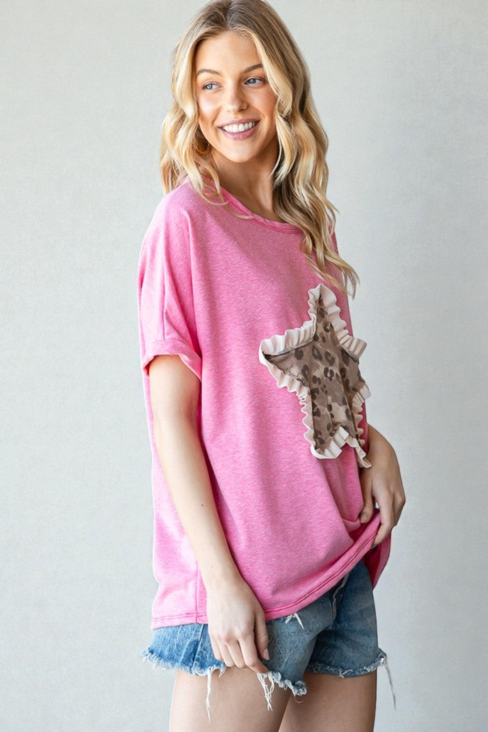 Woman wearing a pink oversized t-shirt with a giraffe design and denim shorts on a plain background
