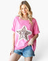 A woman modeling a pink short-sleeve t-shirt with a large ruffled star applique featuring a leopard print pattern on the front, paired with denim shorts against a plain white background.