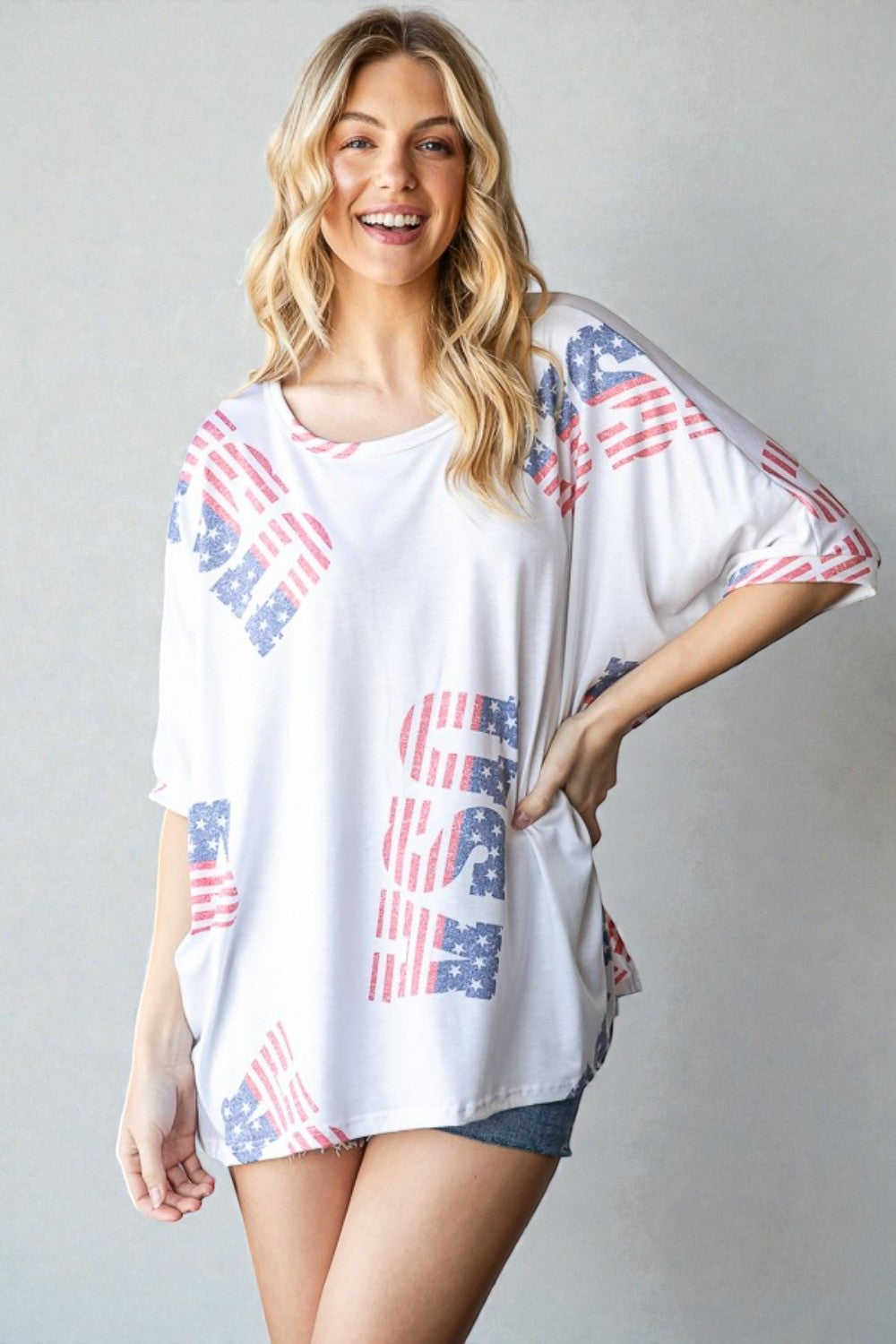 Woman wearing a white oversized shirt with American flag patterns on a plain background