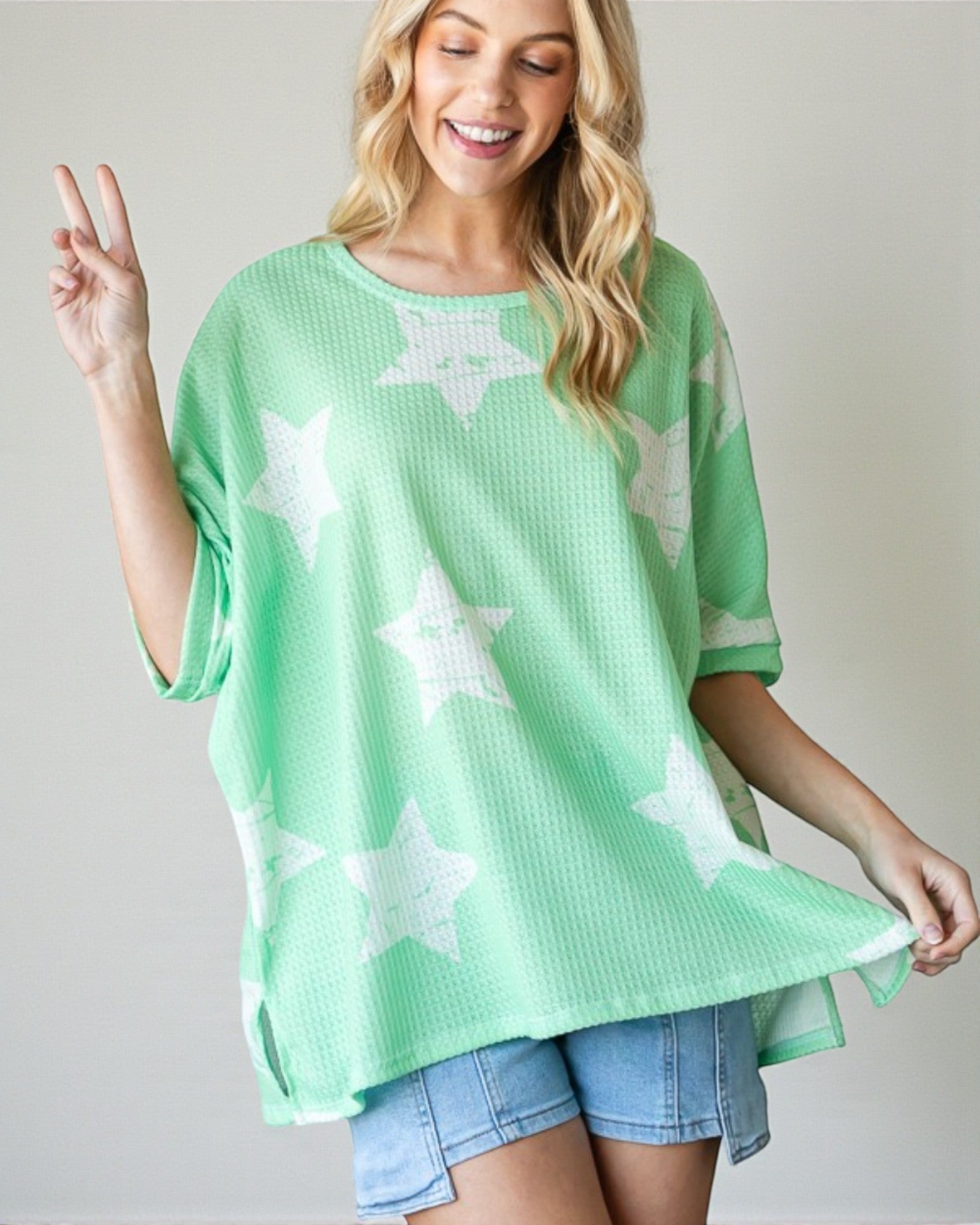 Woman wearing a green oversized t-shirt with star patterns on a plain background