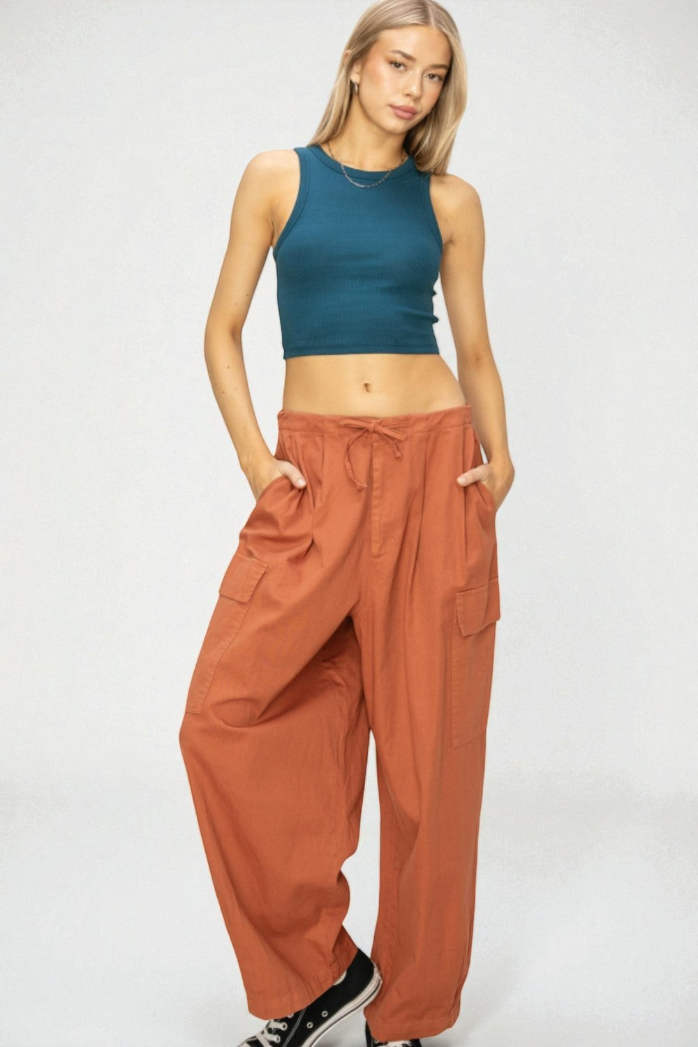Woman wearing a teal crop top and rust-colored pants on a white background