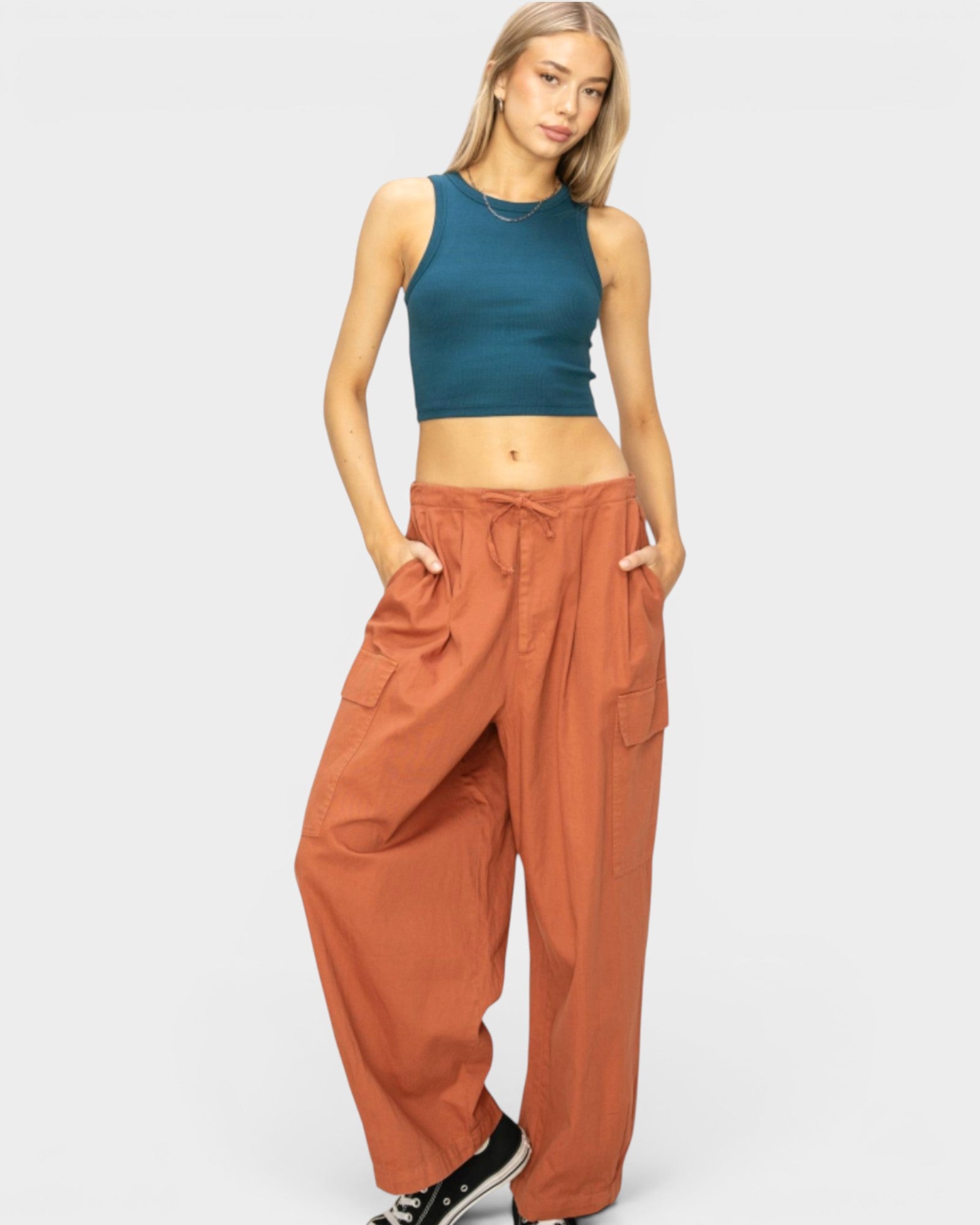 Woman wearing a teal crop top and rust-colored wide-leg pants on a white background