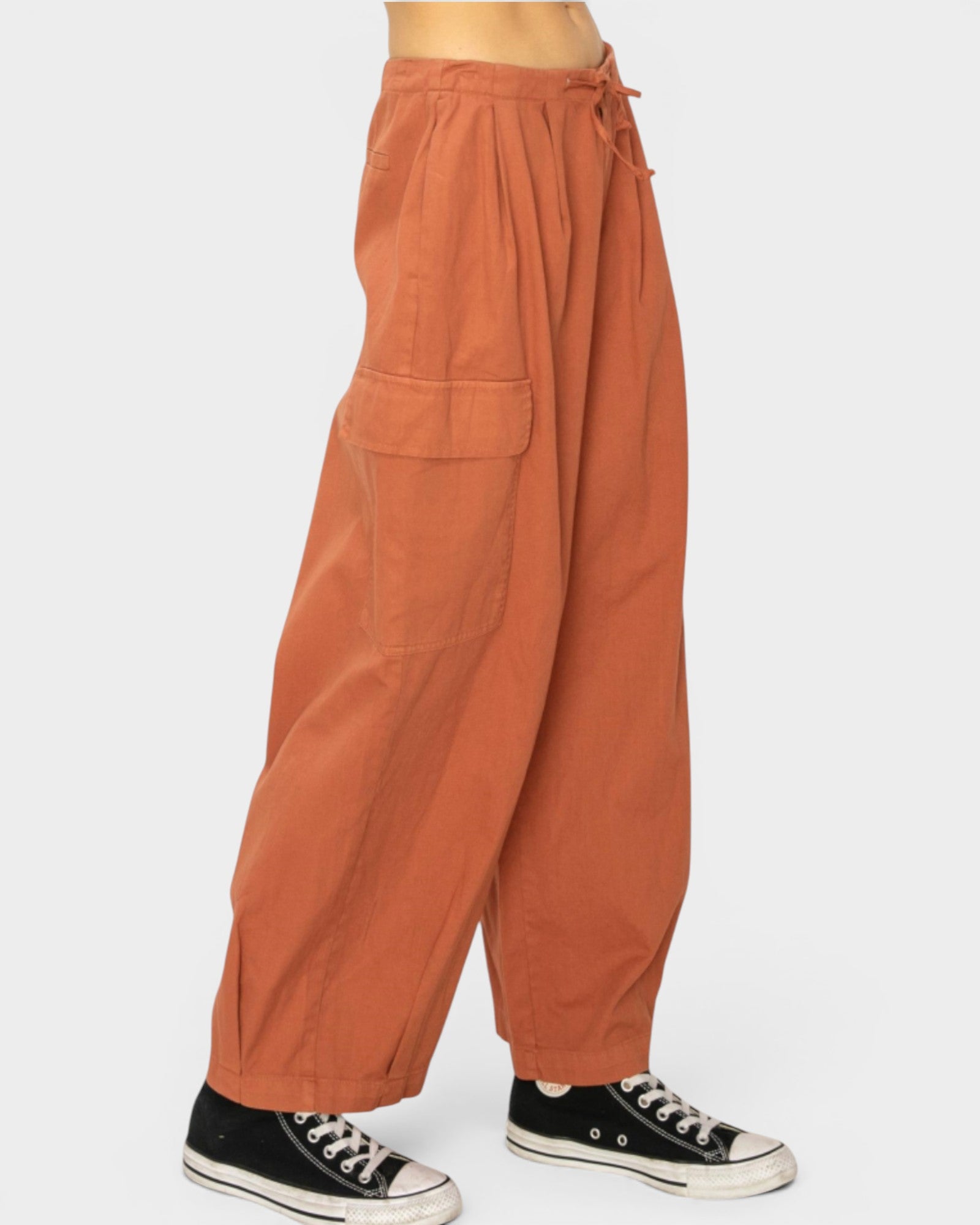 Copper-colored wide-leg pants worn with black Converse shoes on a white background