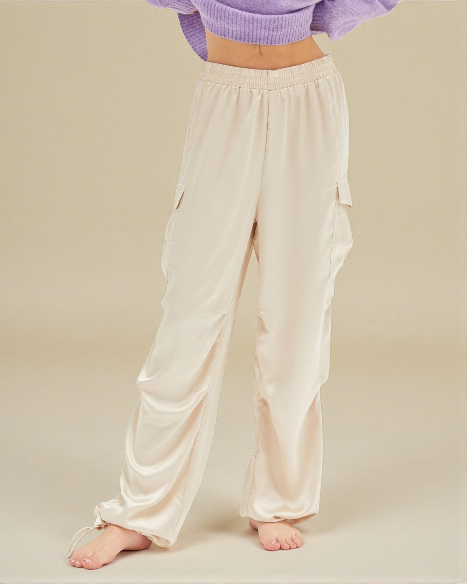Person wearing cream satin pants on a beige background