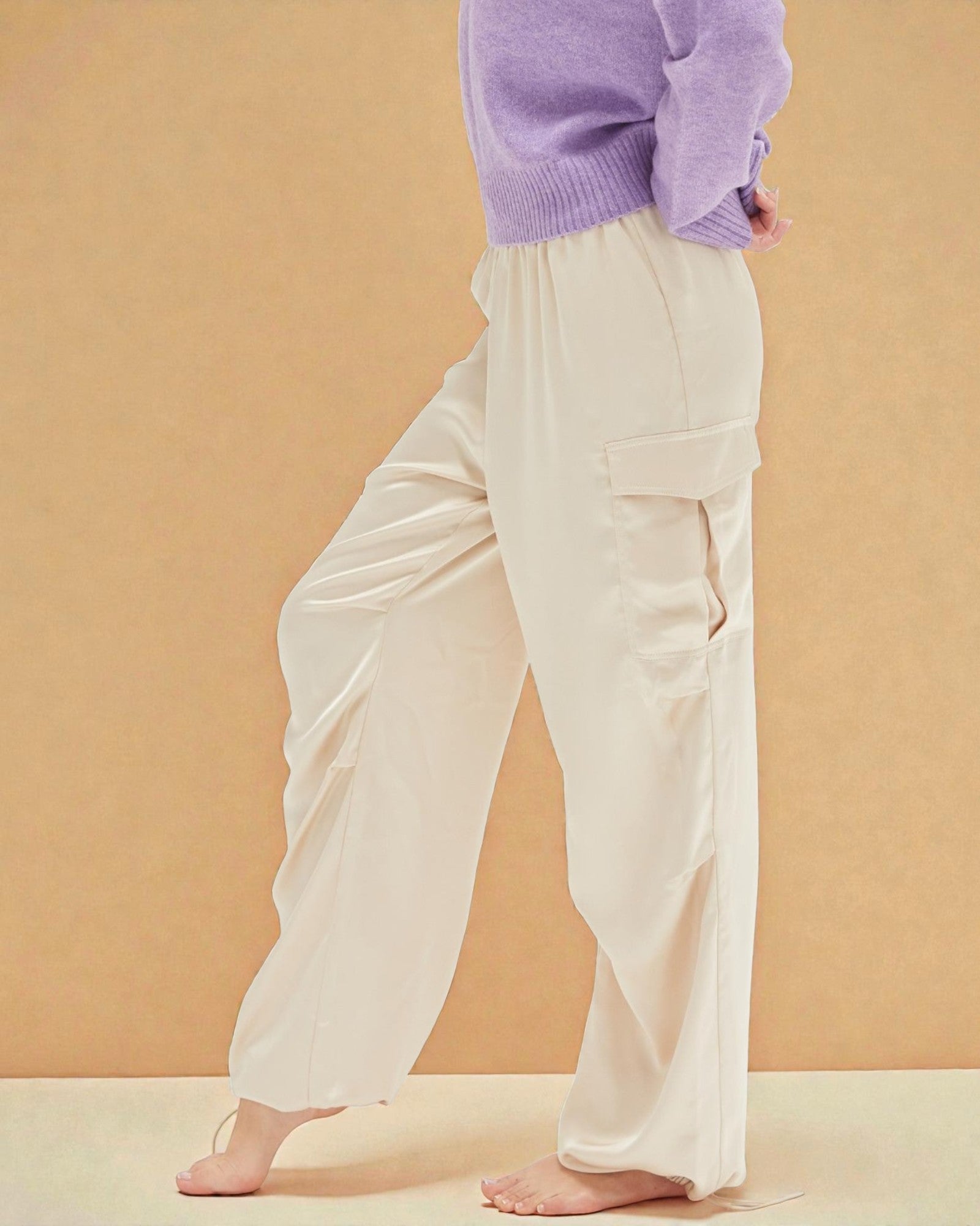 Person wearing white cargo pants and a purple sweater on a beige background