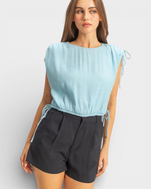 Woman wearing a light blue sleeveless top and black shorts on a white background