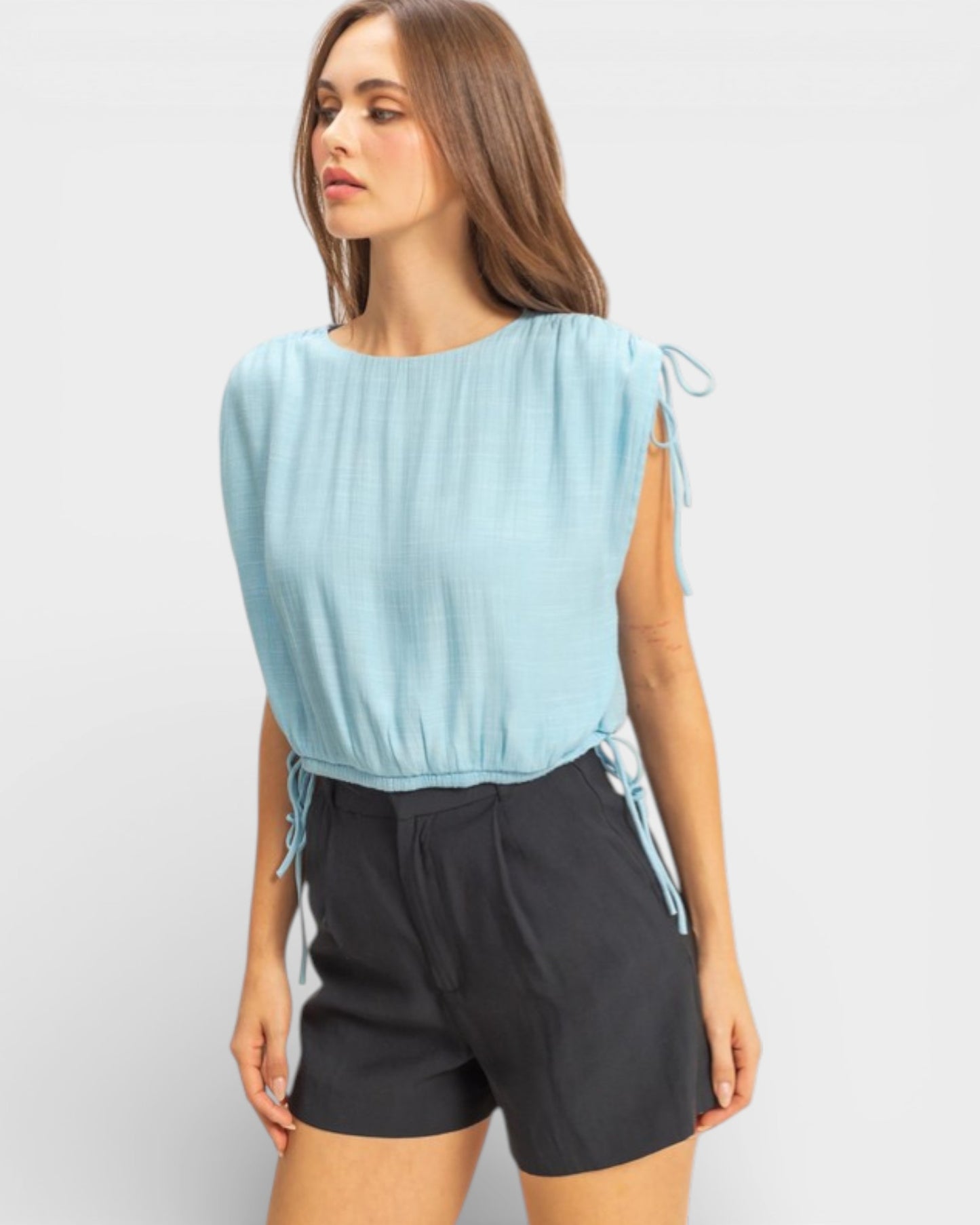 Woman wearing a light blue sleeveless top and black shorts on a white background