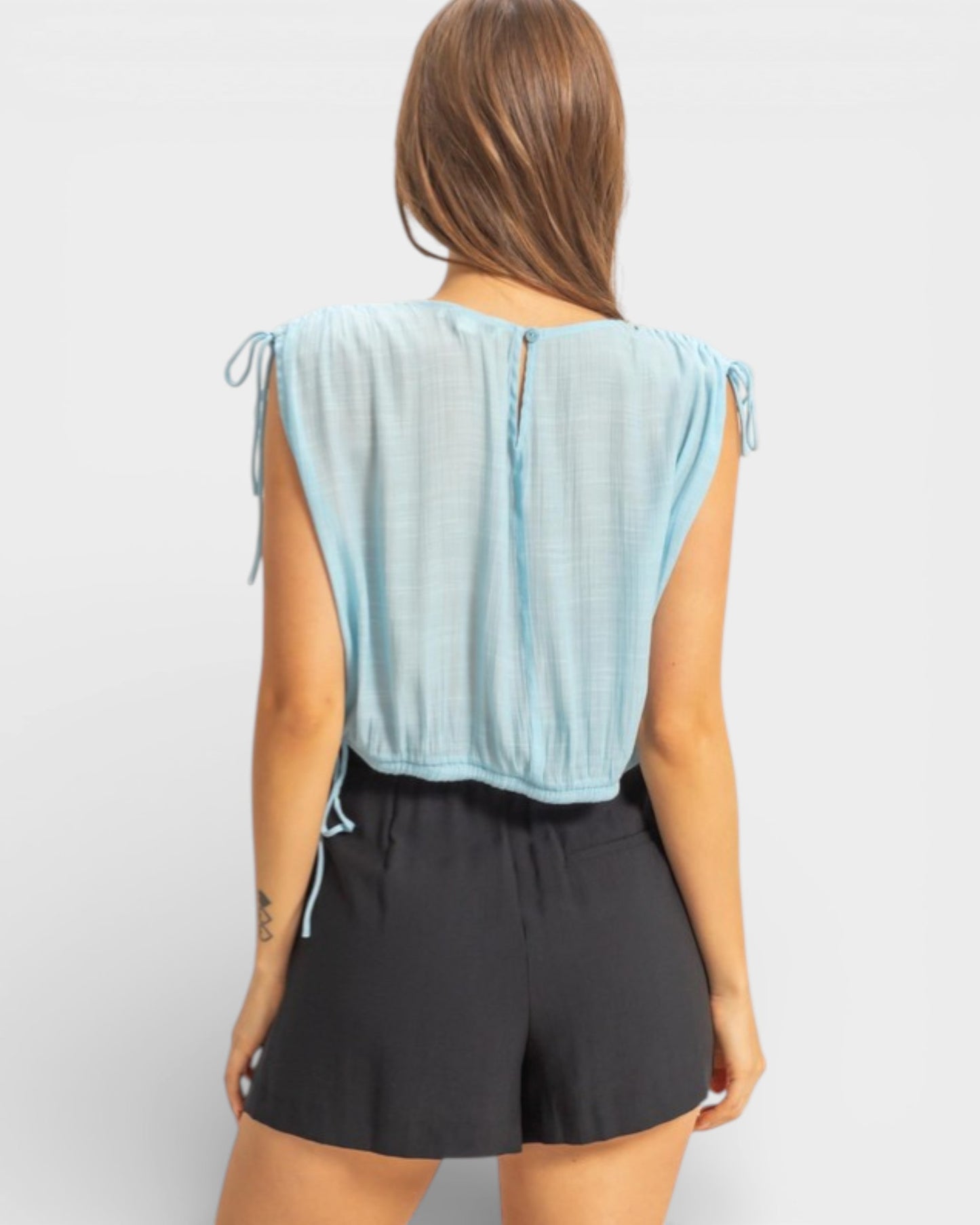 Woman wearing a light blue sleeveless top and black shorts on a white background