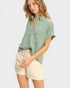 Woman wearing a light green button-up shirt and beige shorts on a white background