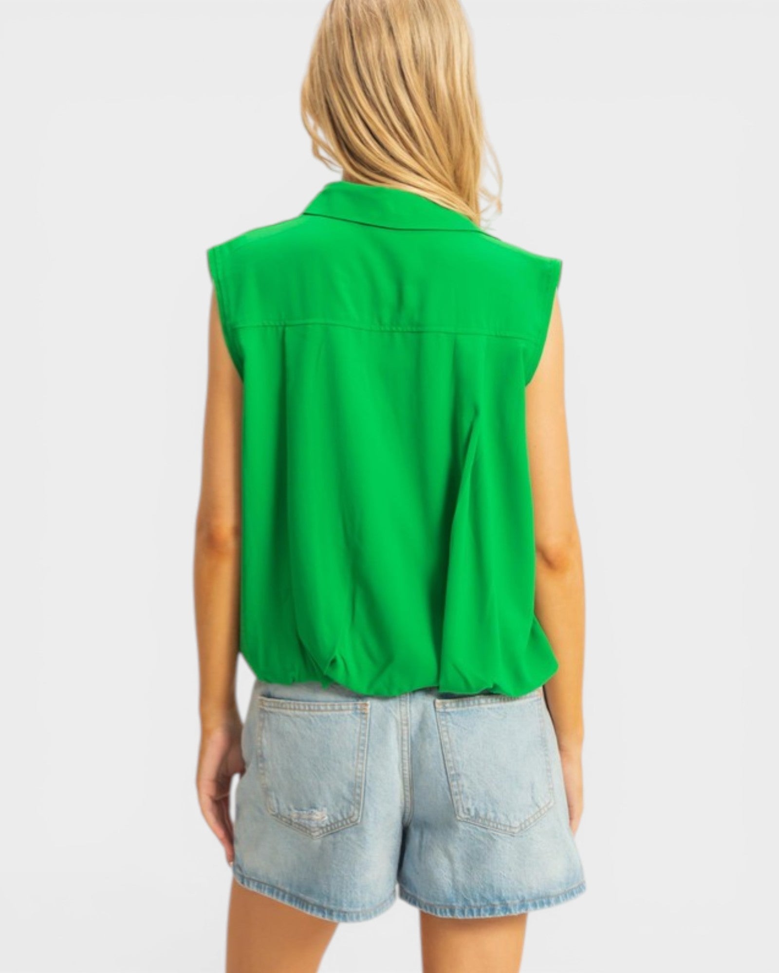 Person wearing a green sleeveless top and denim shorts on a white background