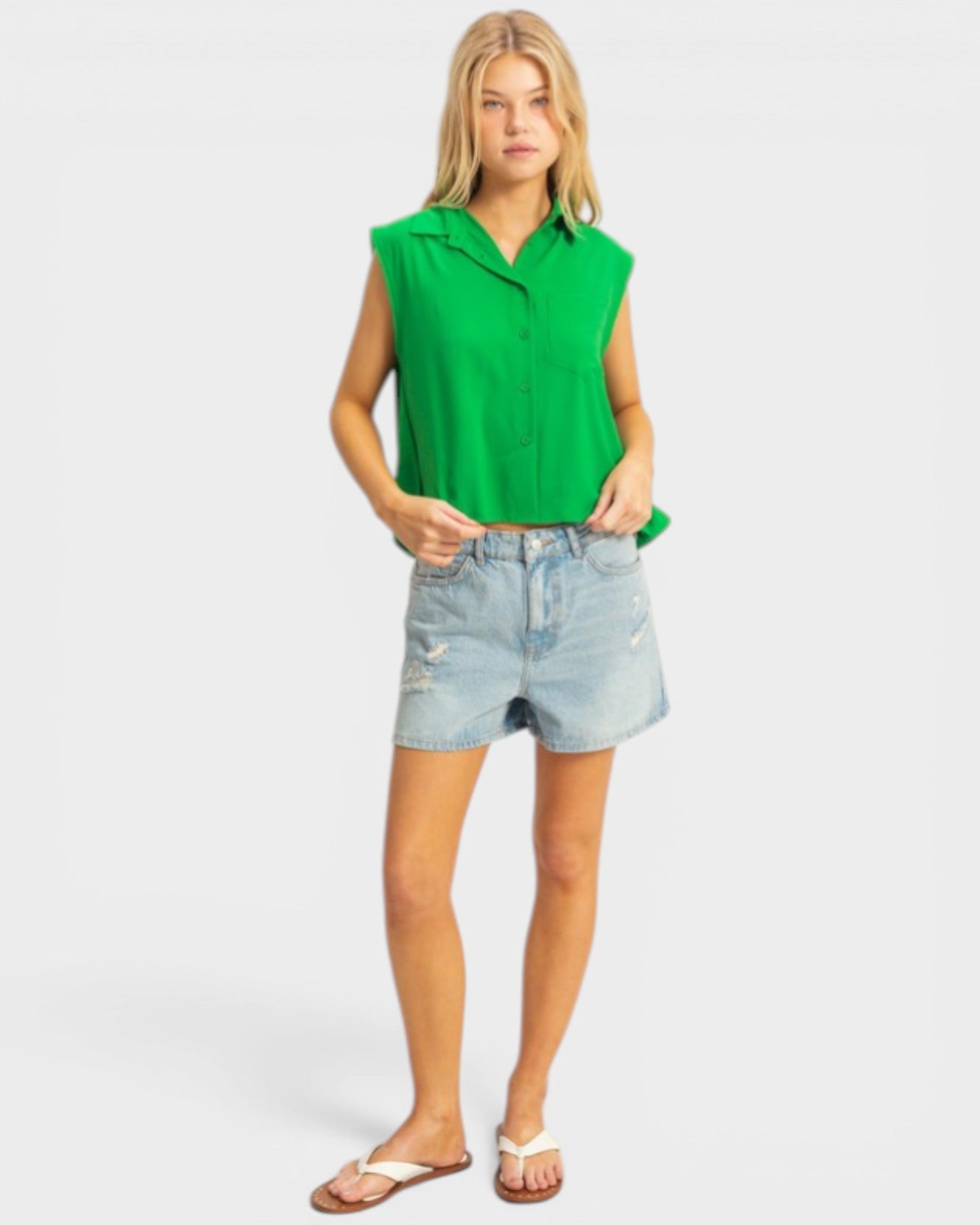 Woman wearing a green sleeveless top and denim shorts on a white background