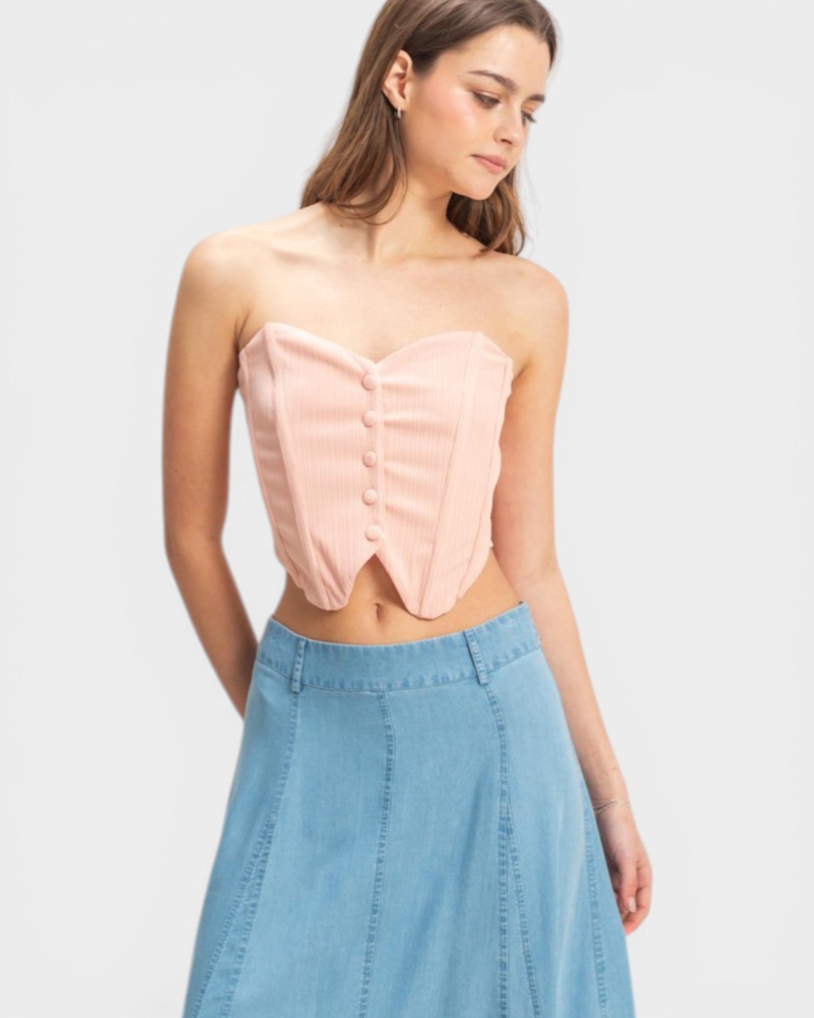 Woman wearing a strapless pink top and denim skirt on a light gray background