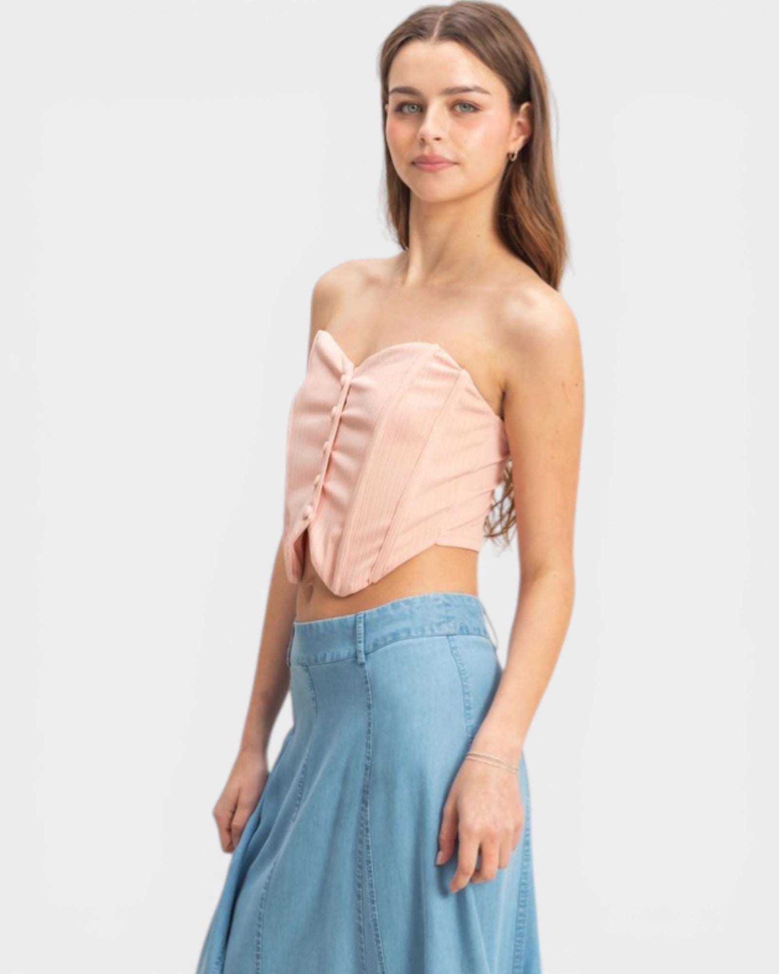 Woman wearing a strapless pink top and denim skirt on a white background