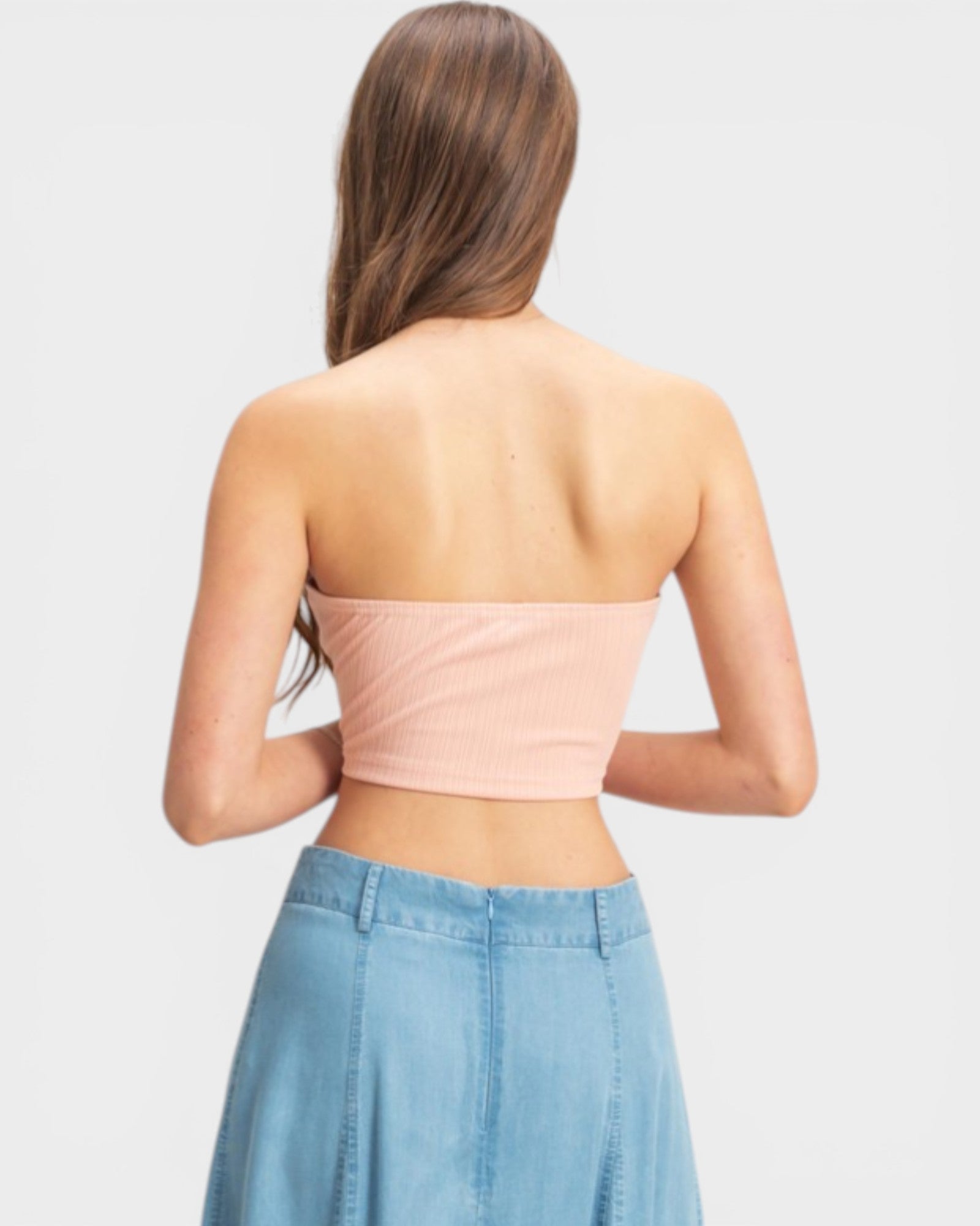 Woman wearing a strapless pink top and denim skirt on a light gray background