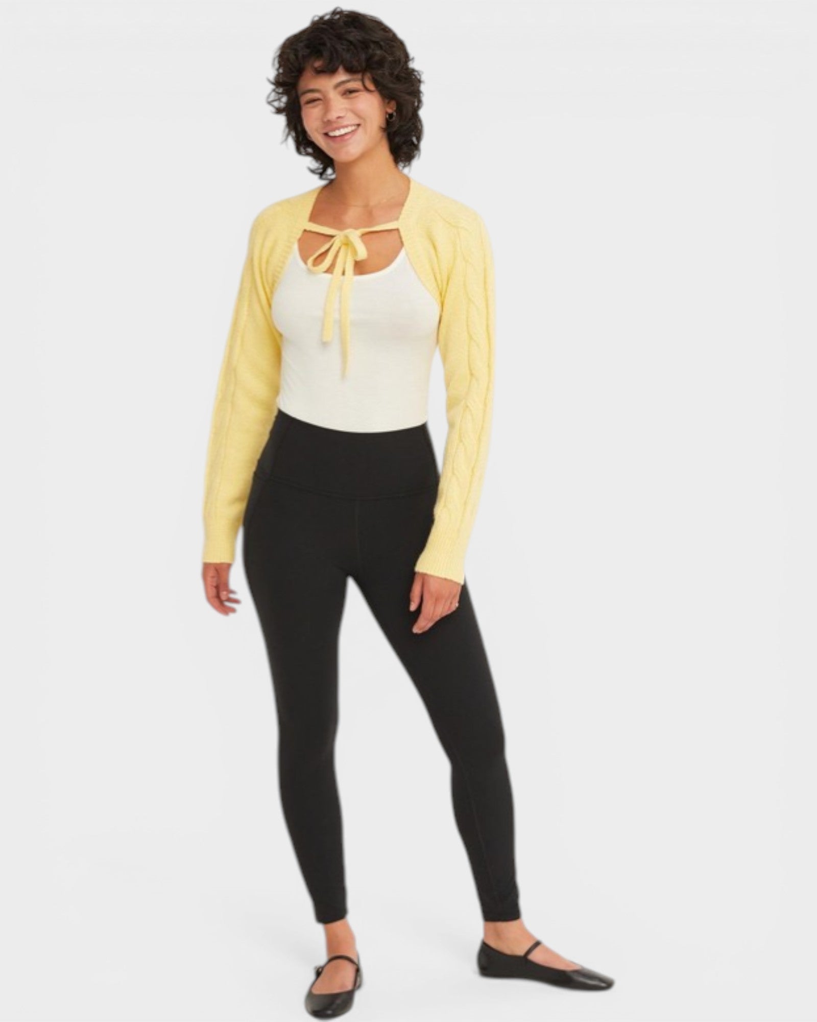 Woman wearing a yellow cardigan, white top, and black leggings on a white background